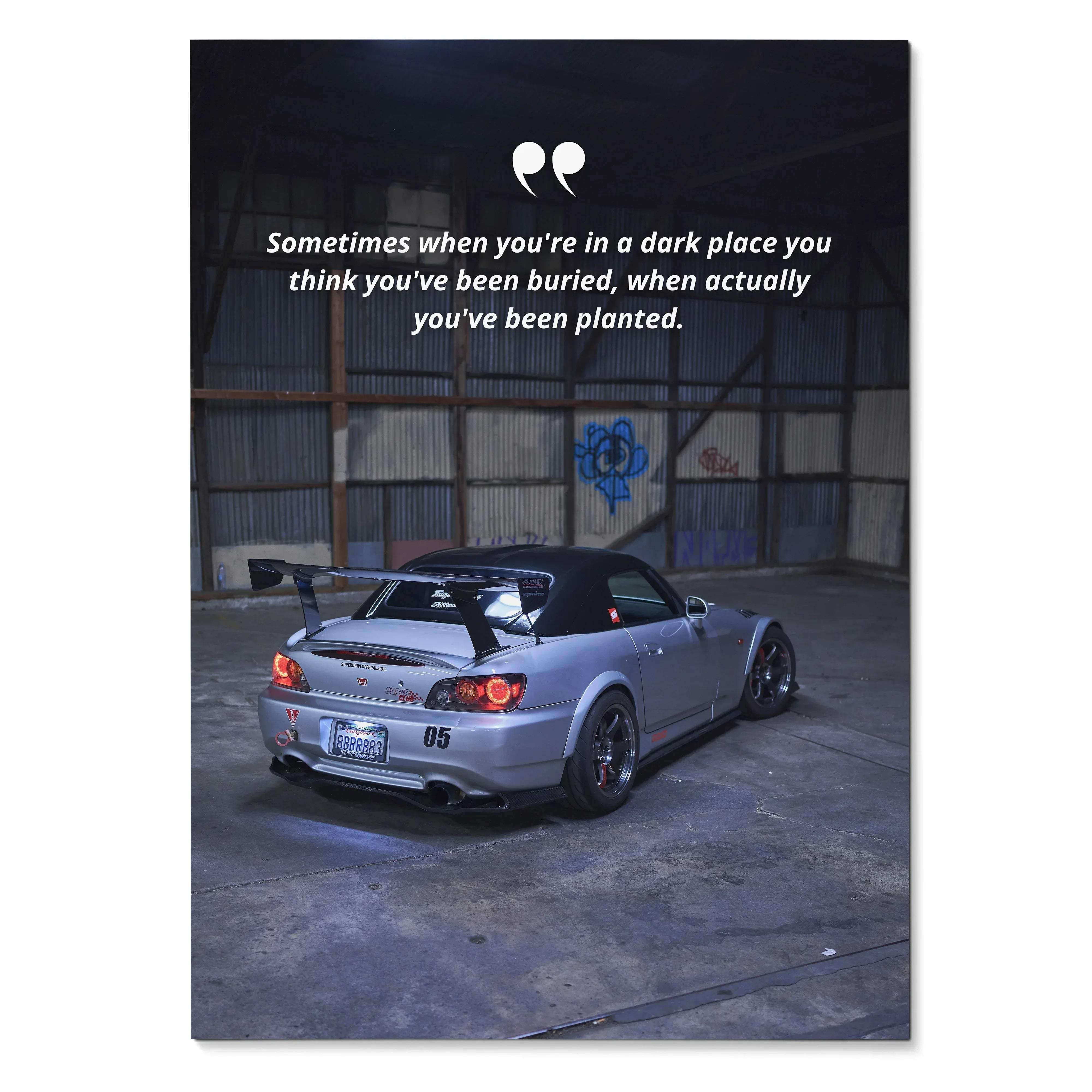 Silver Honda S2000 sports car with black soft top and rear spoiler parked in industrial-style garage motivational poster