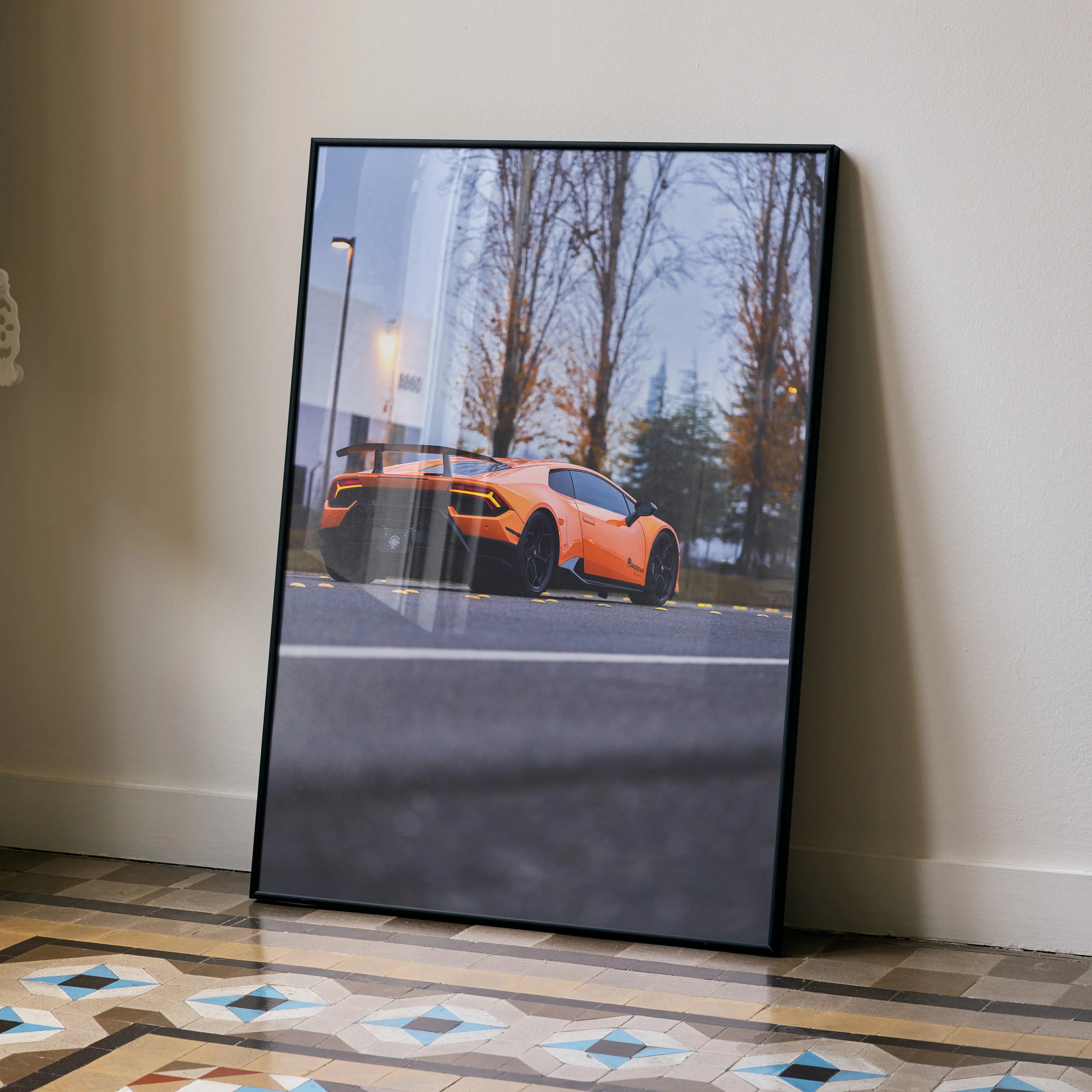 Lamborghini Huracan orange sports car poster wall art in black frame leaning on beige wall.