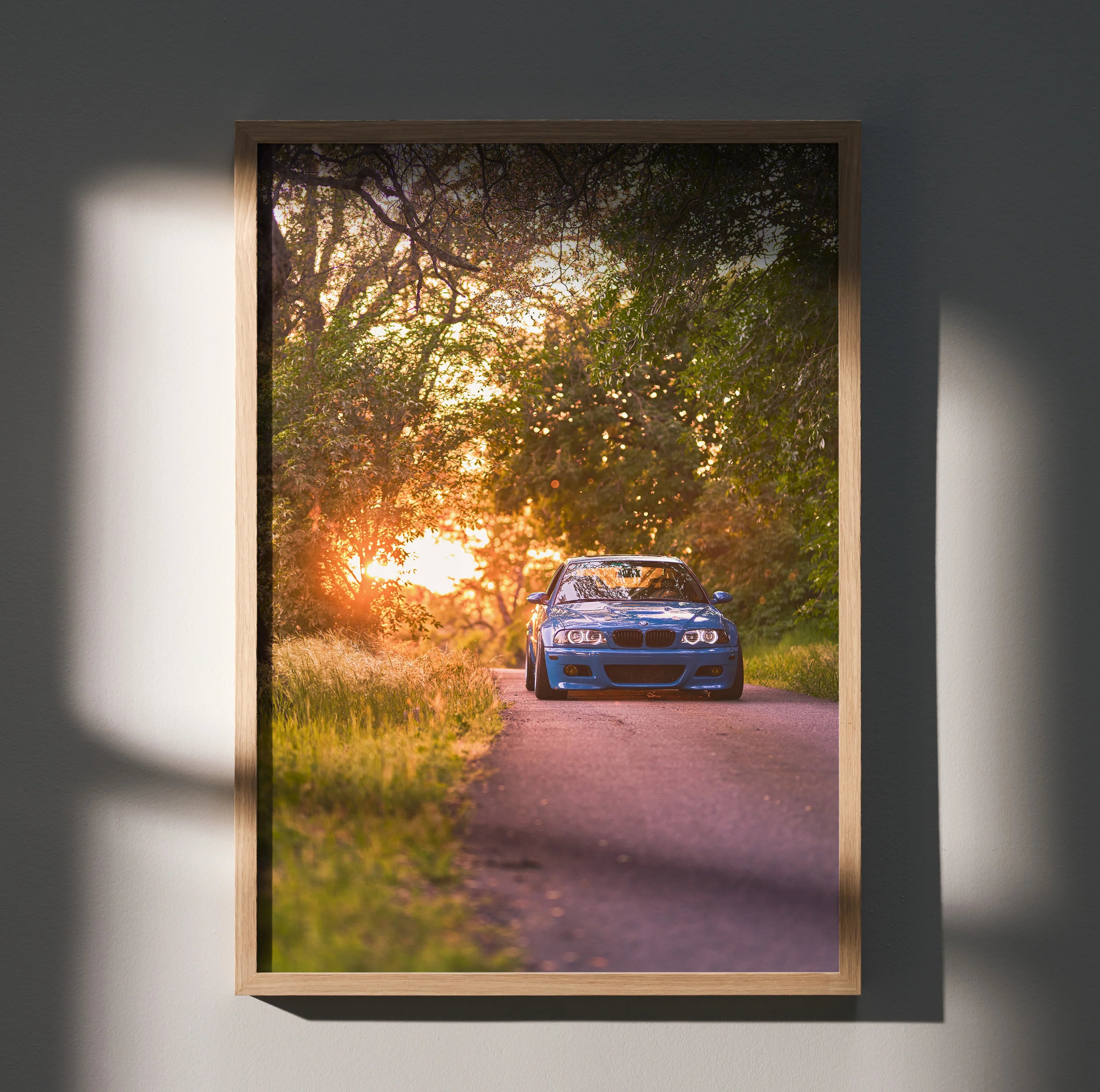 BMW E46 M3 poster with sunset behind car on tree-lined road, automotive wall art.