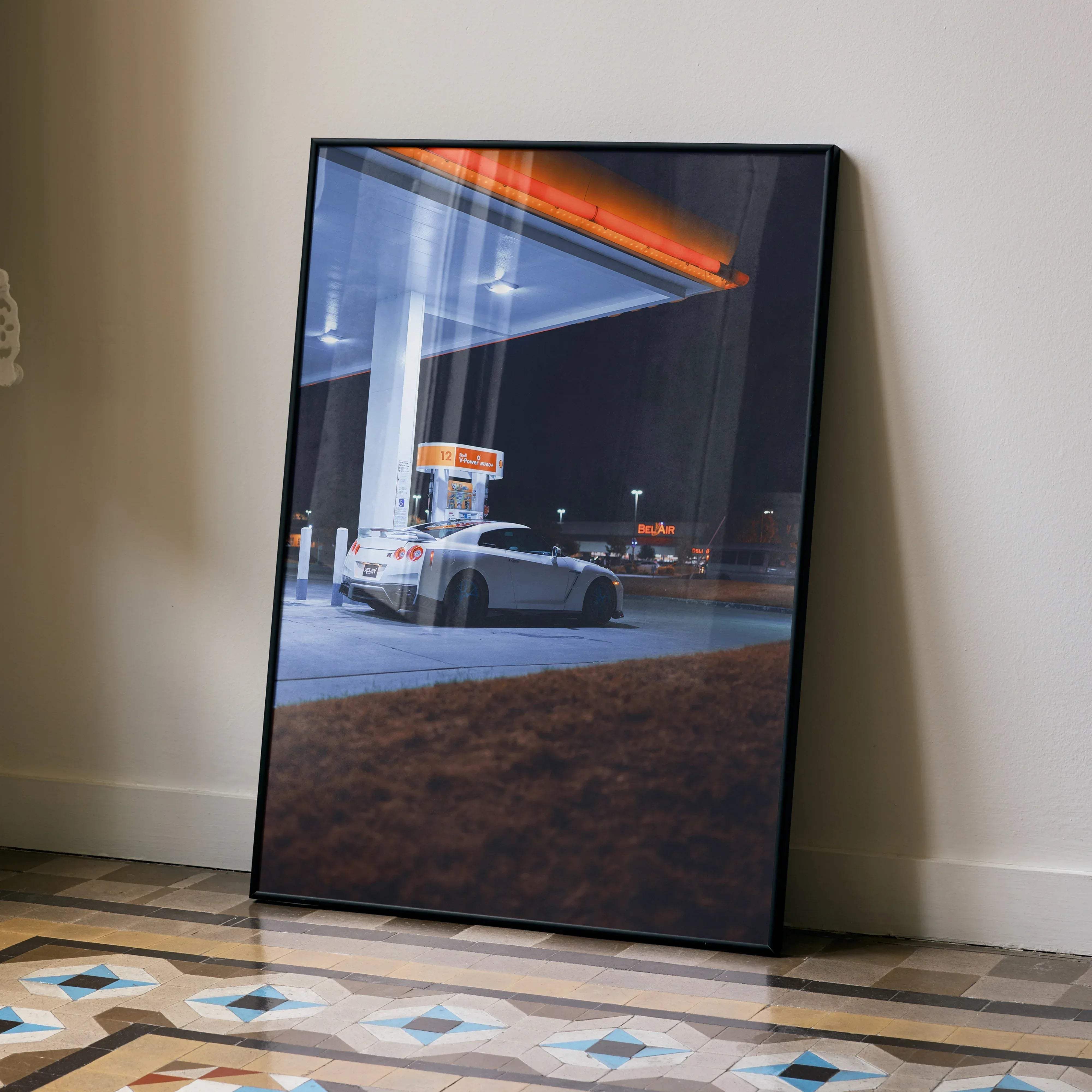 Black-framed art print of a white nissan gtr r35 sports car at a gas station under nighttime lighting