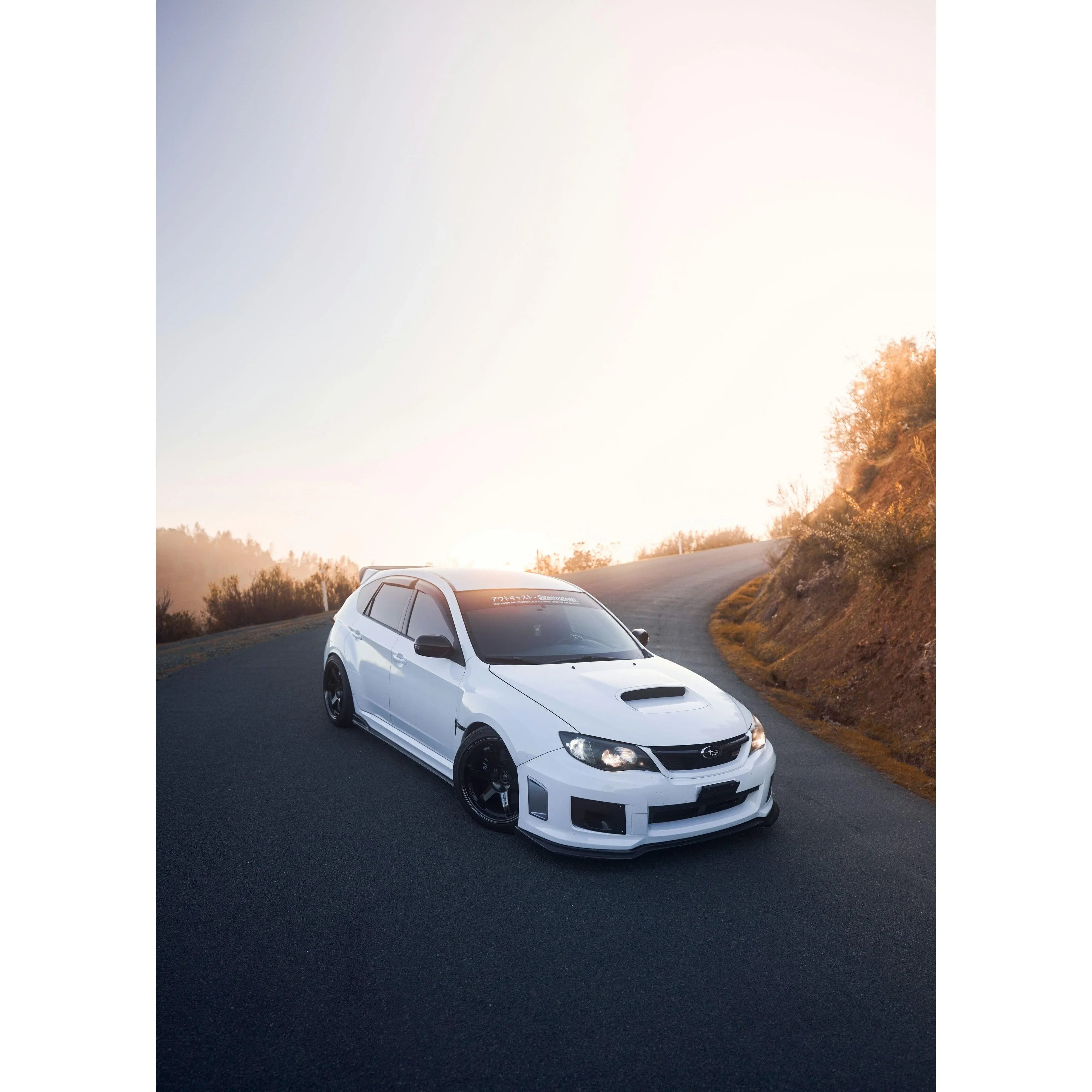 White Subaru WRX STI parked on winding road at sunrise poster wall art.