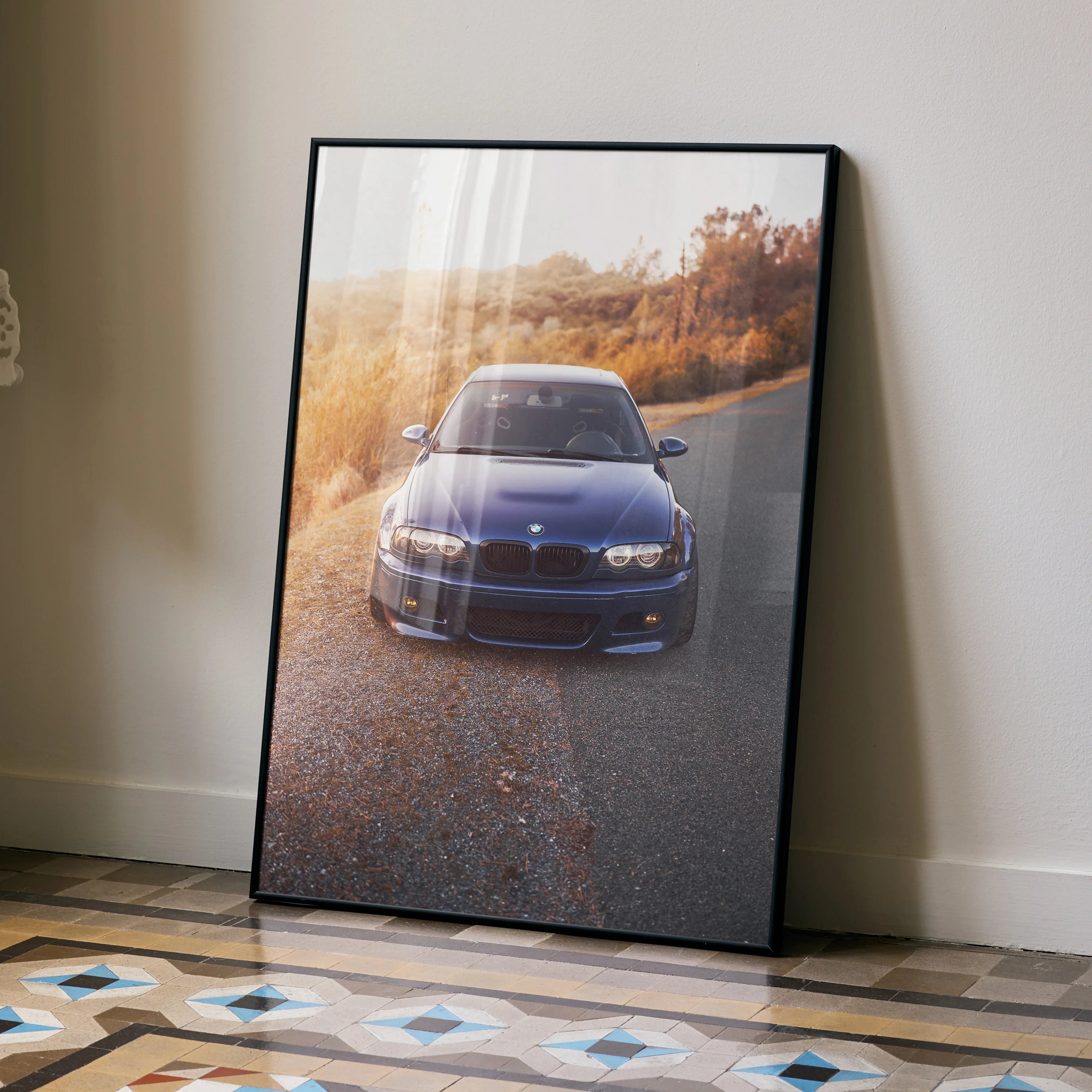 BMW E46 M3 poster wall art with a blue car on a scenic road during golden hour in a black frame.