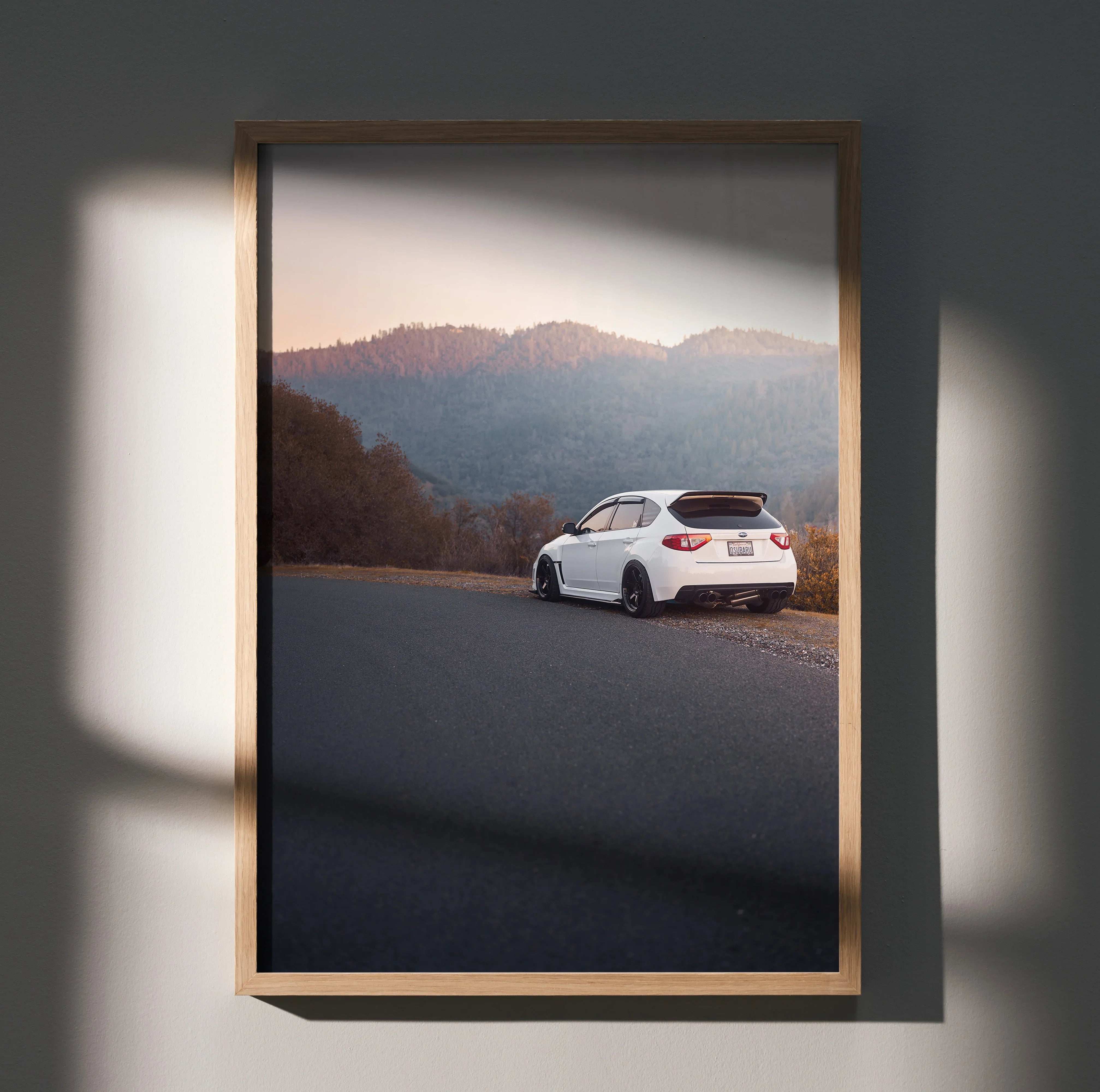 Subaru WRX STI driving on mountain road at sunset poster wall art in wooden frame.