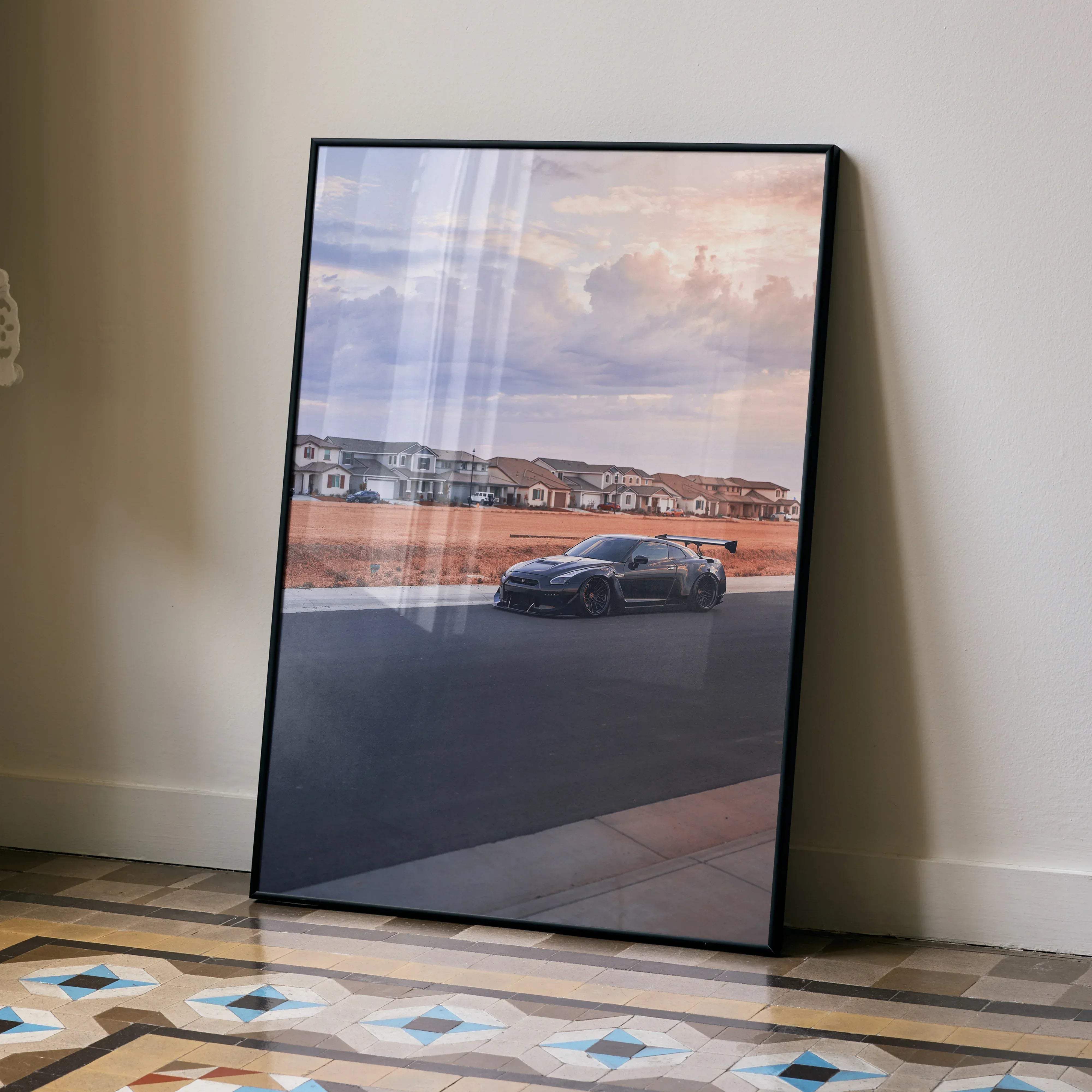 Black-framed poster of matte black nissan r35 gtr widebody with rear wing on asphalt under pink gray sky wall art