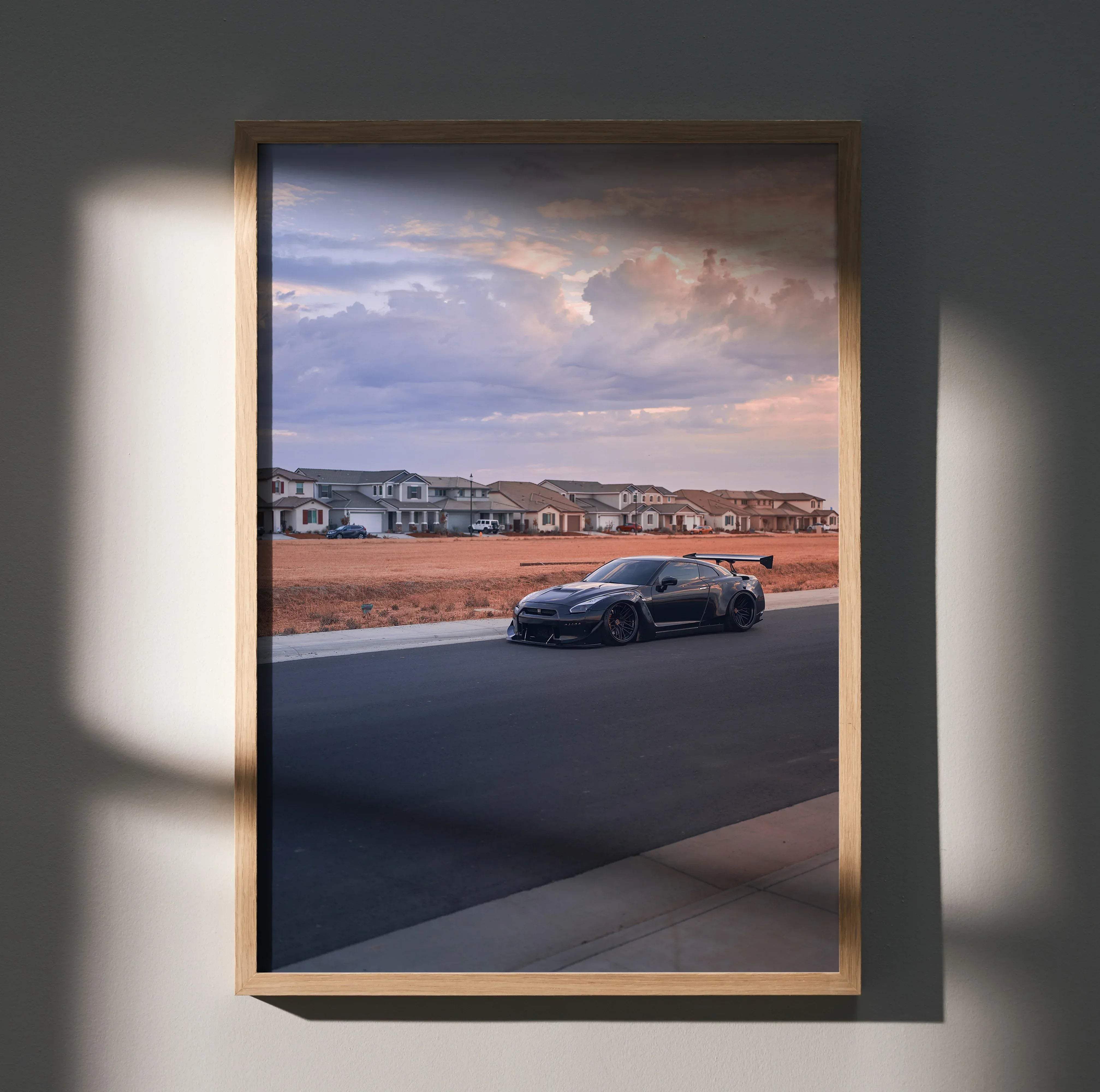 A framed high resolution art print of a black Nissan R35 GT-R widebody parked on a suburban street under dramatic sky