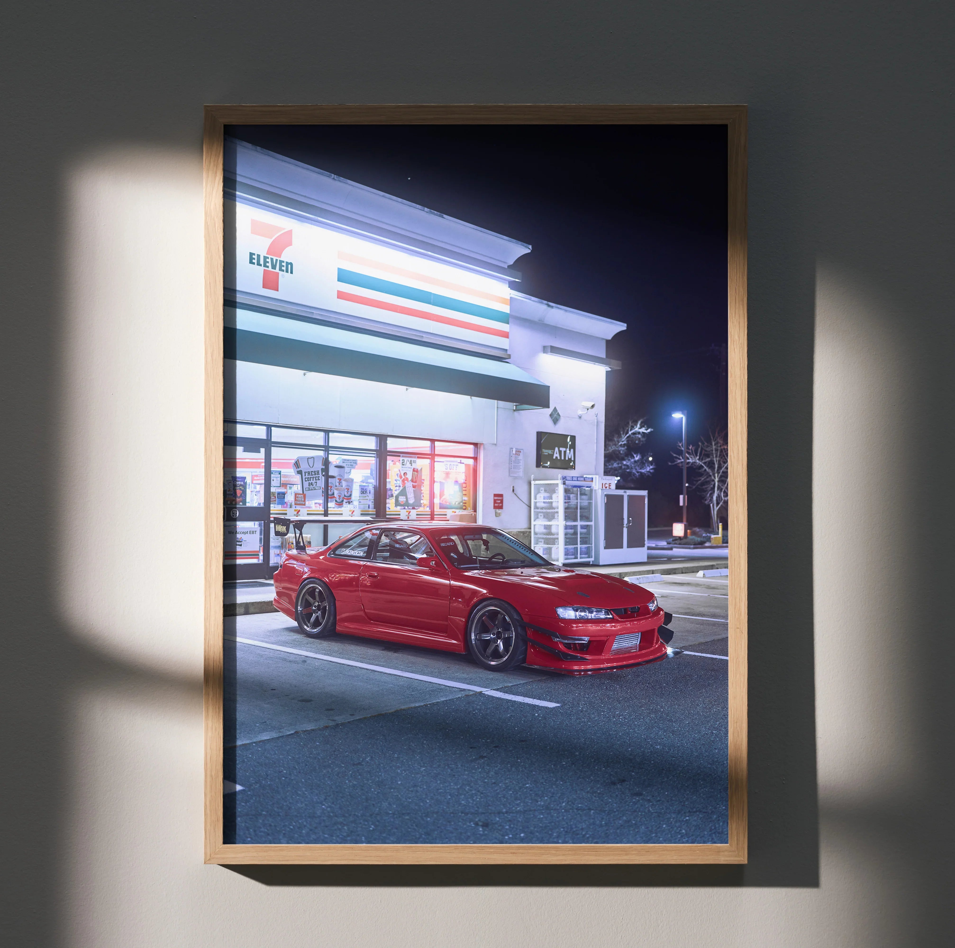 Red Nissan 240sx S14 Kouki parked in front of a brightly lit convenience store, poster wall art in wooden frame.