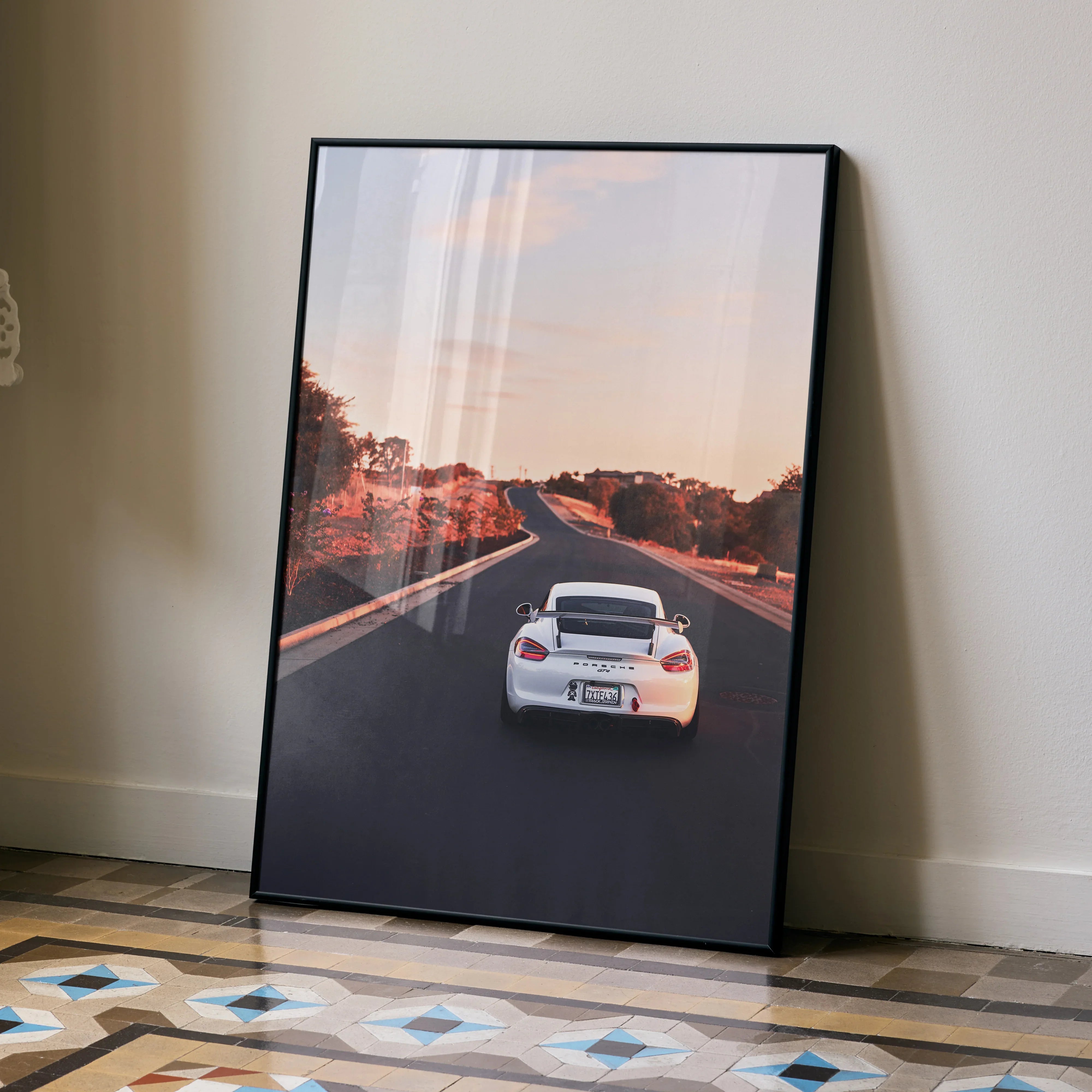 Porsche Cayman GT4 driving on road at sunset poster wall art in black frame.
