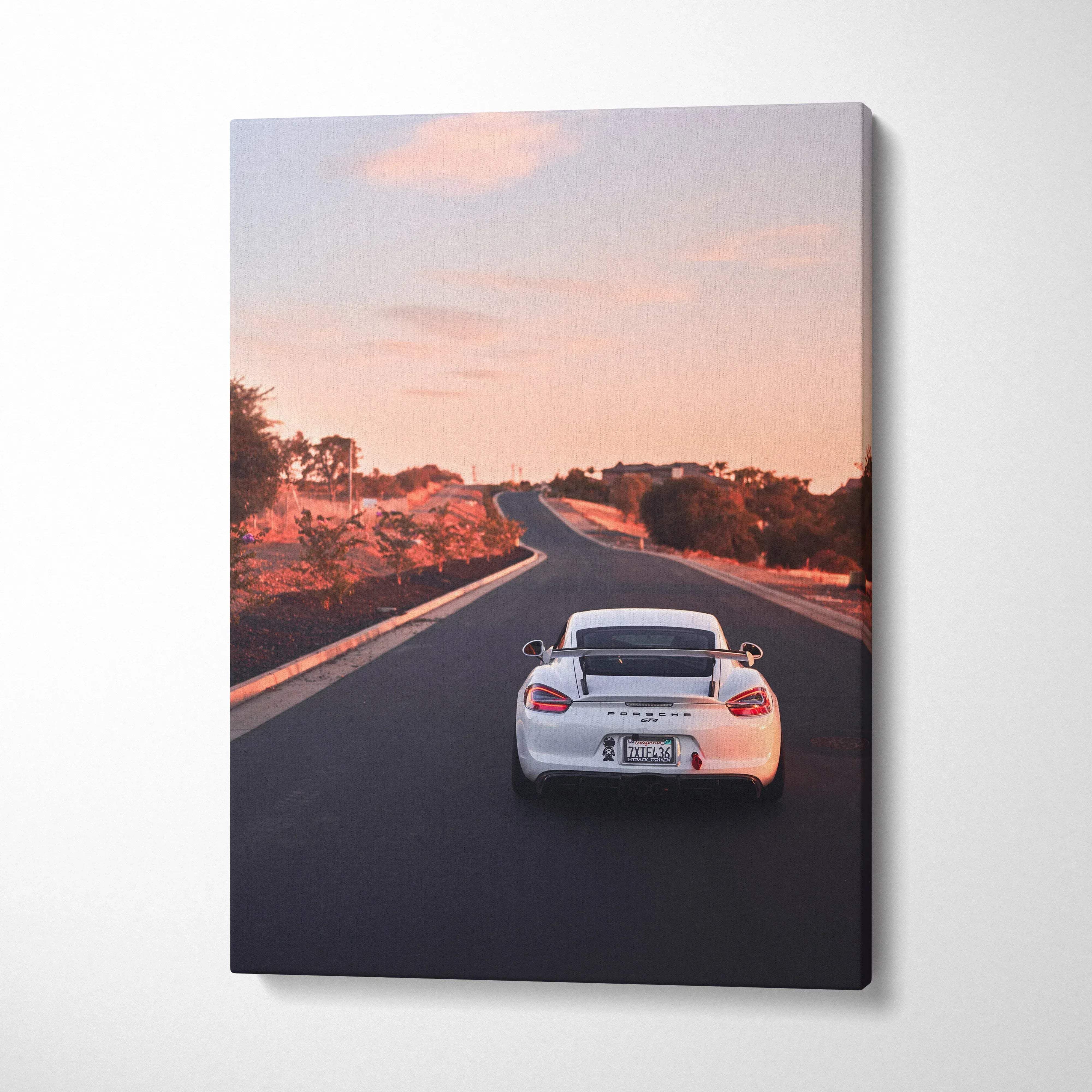 Vertical canvas wall art featuring white Porsche GT4 driving on an empty road at sunset.