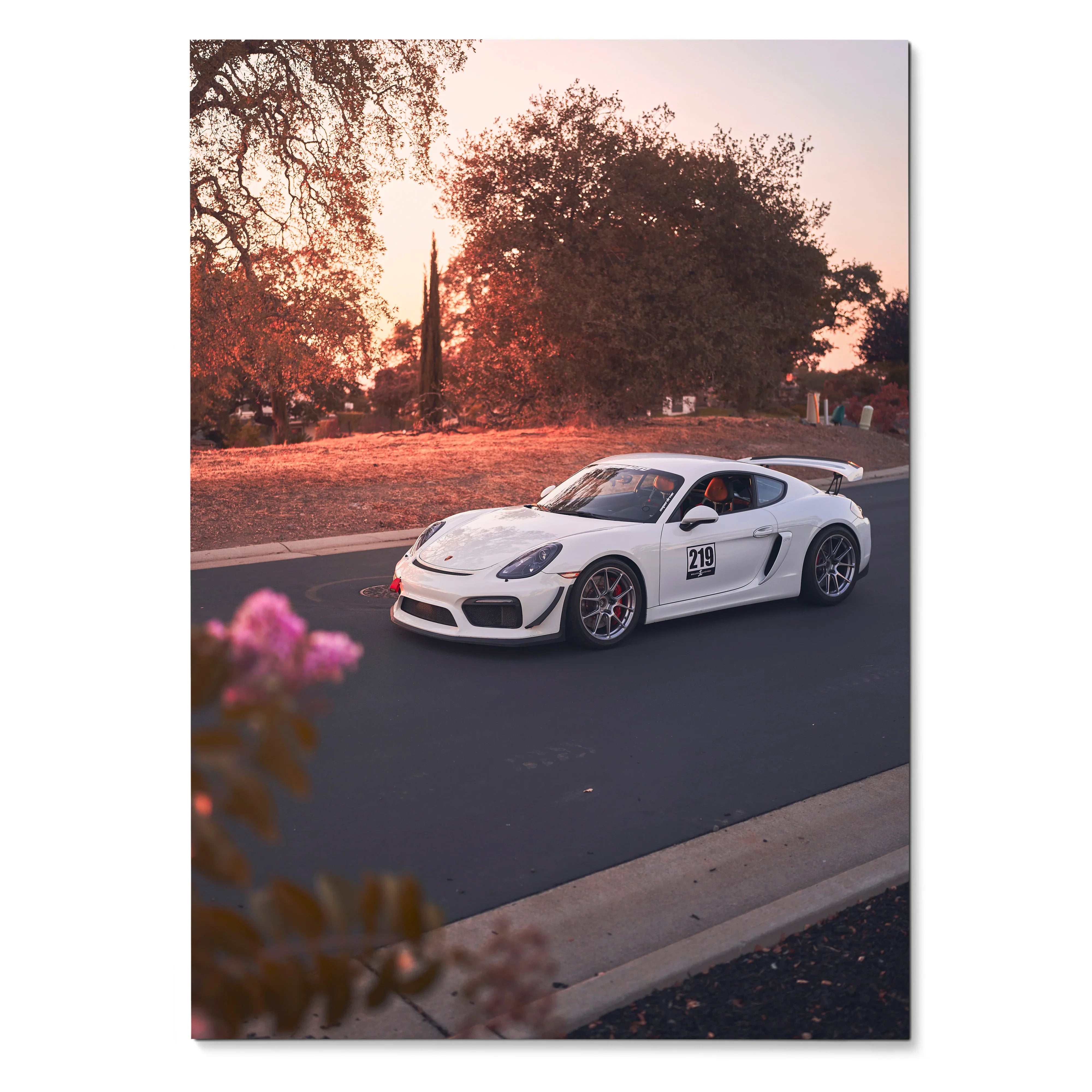 Porsche Cayman GT4 racing on road at sunset poster wall art with warm orange sky and trees.