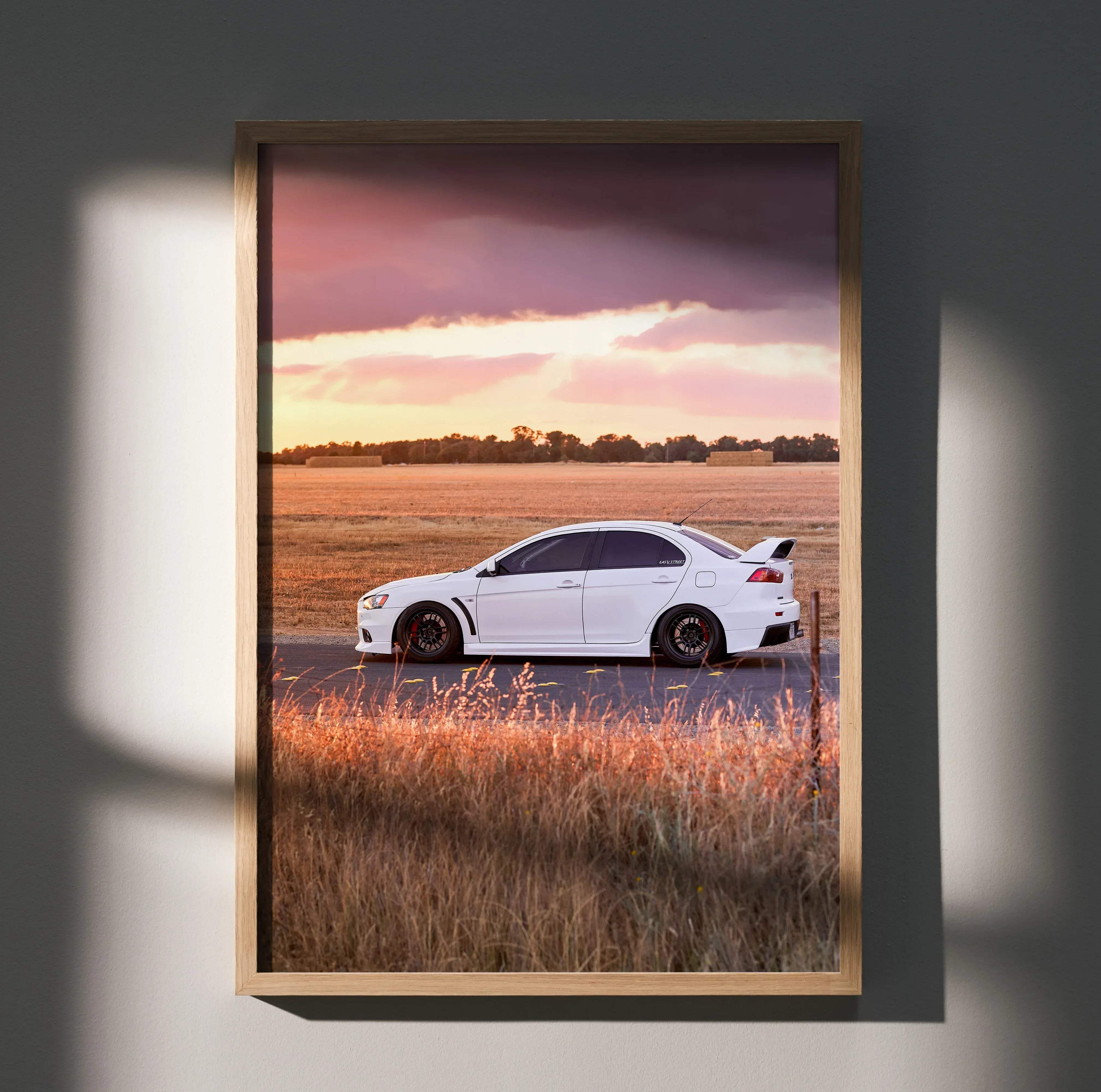 A framed high resolution poster of a white Mitsubishi Evo 10 parked in a field at sunset with dramatic skies
