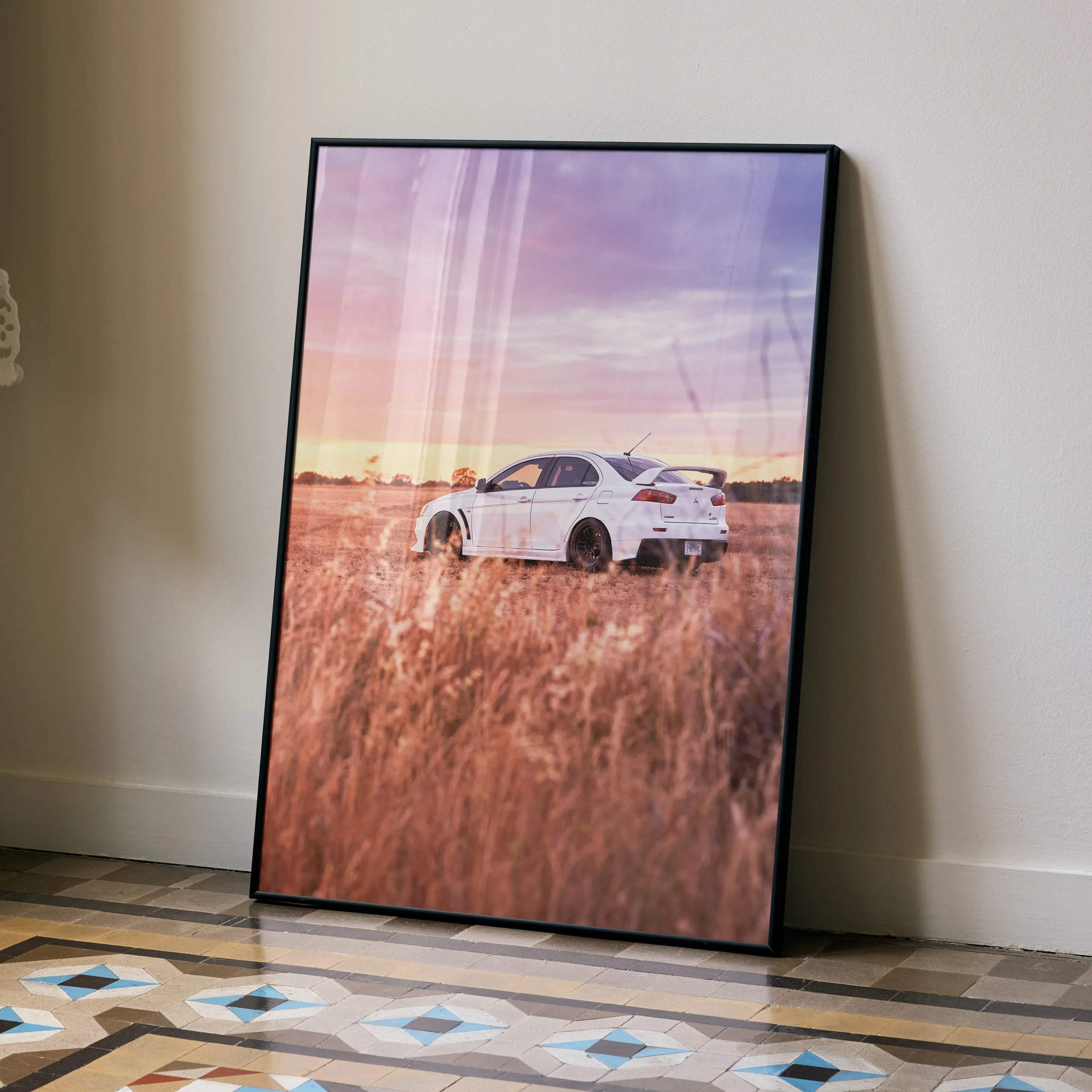 A framed poster of a white mitsubishi evo 10 sports car in a golden field under a pink and purple sky