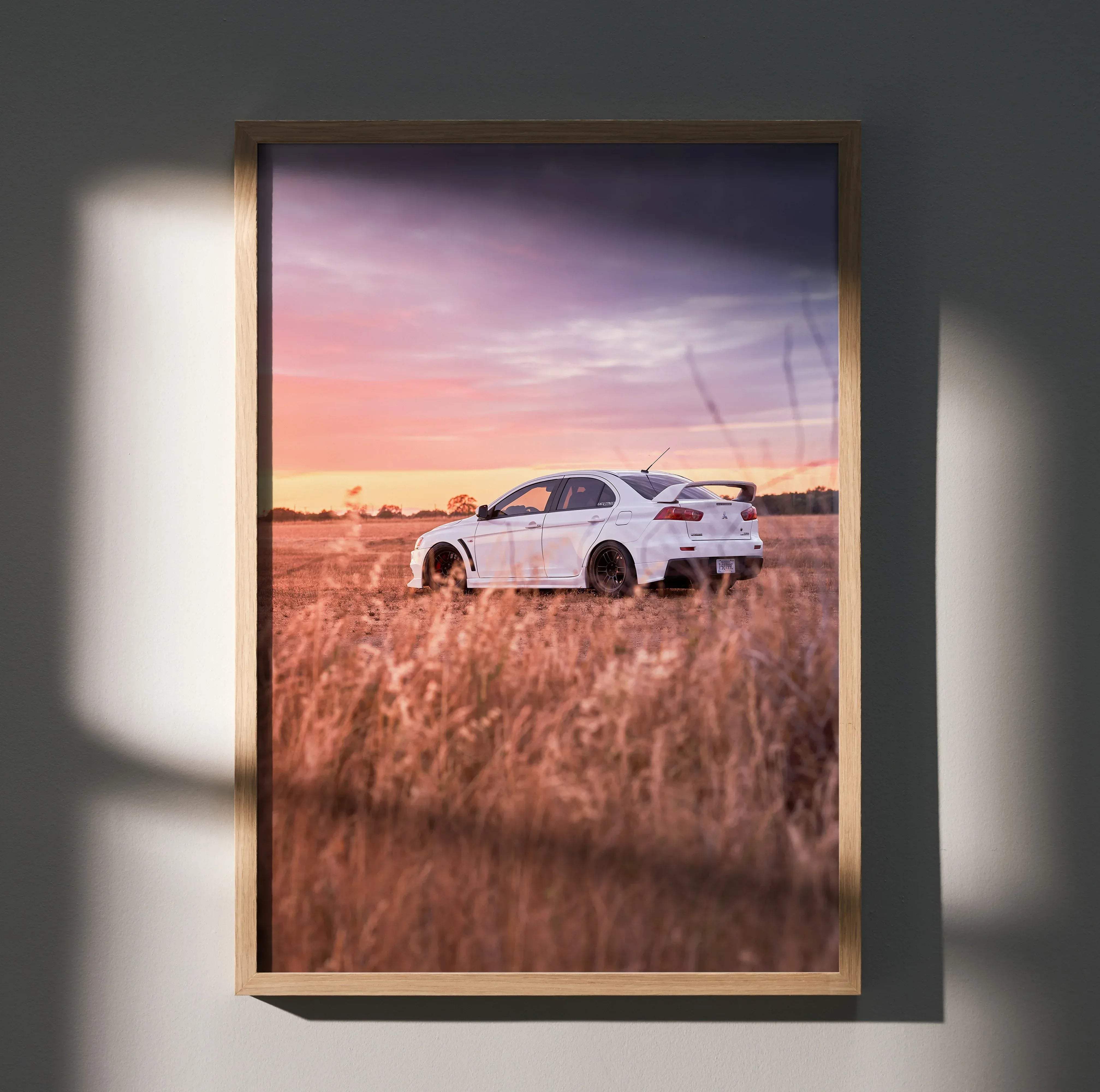 Framed print of a white mitsubishi lancer evolution sports car parked in tall golden grass under twilight sky