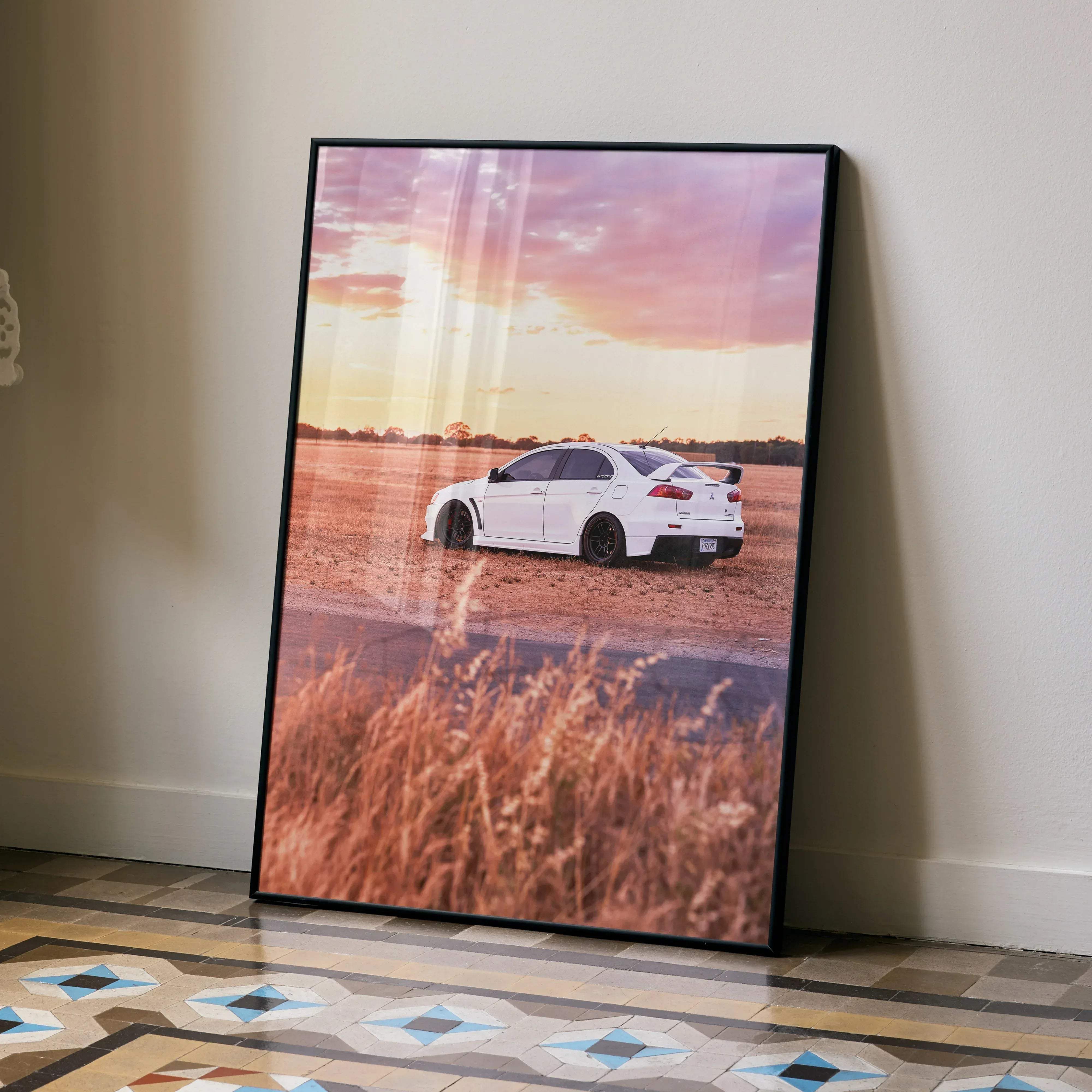 A framed poster of a white Mitsubishi Evo 10 sports car parked in a field at sunset with a black frame