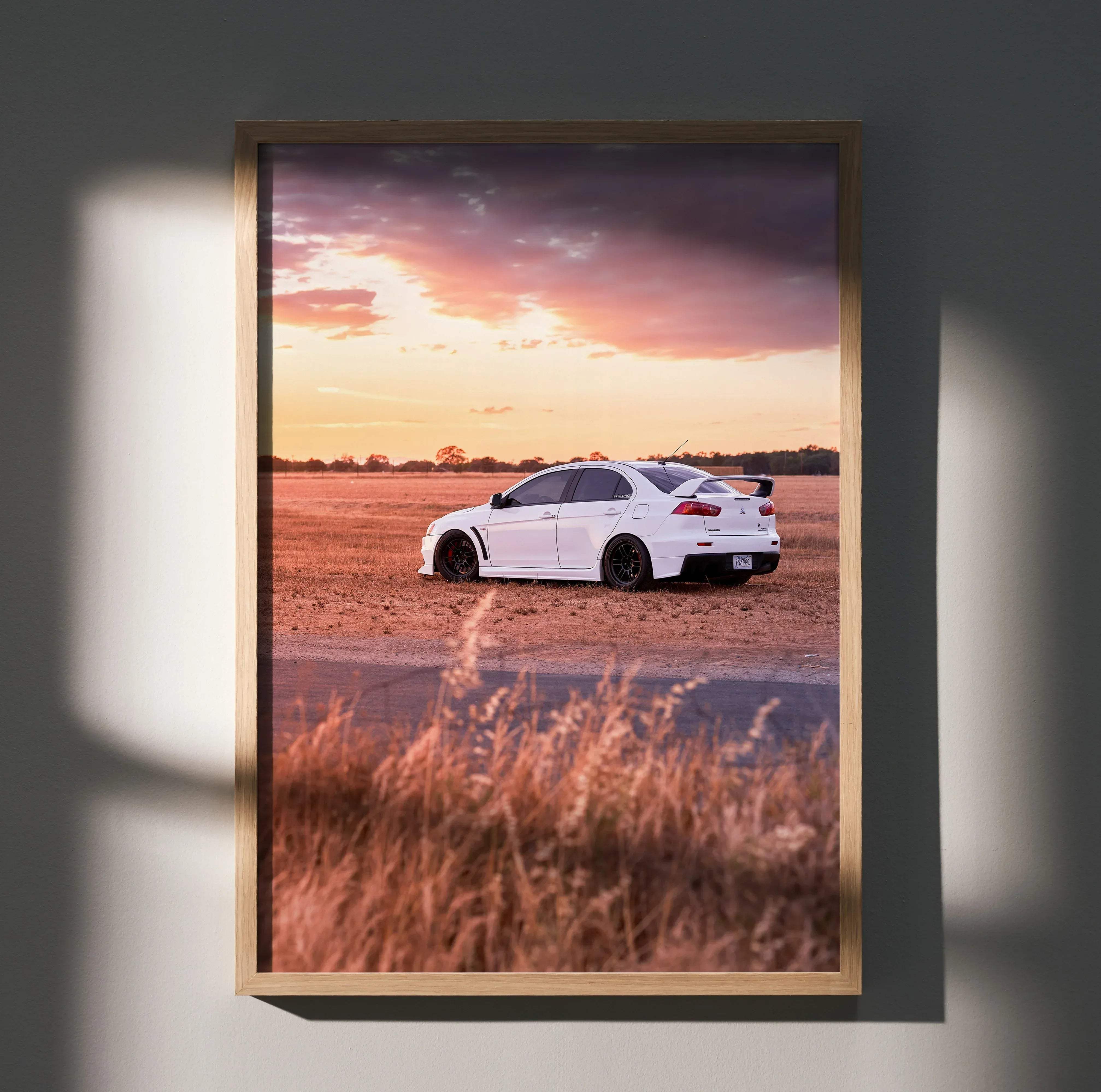 White Mitsubishi Evo 10 sports car with black rims and rear spoiler in an open field at sunset high resolution poster