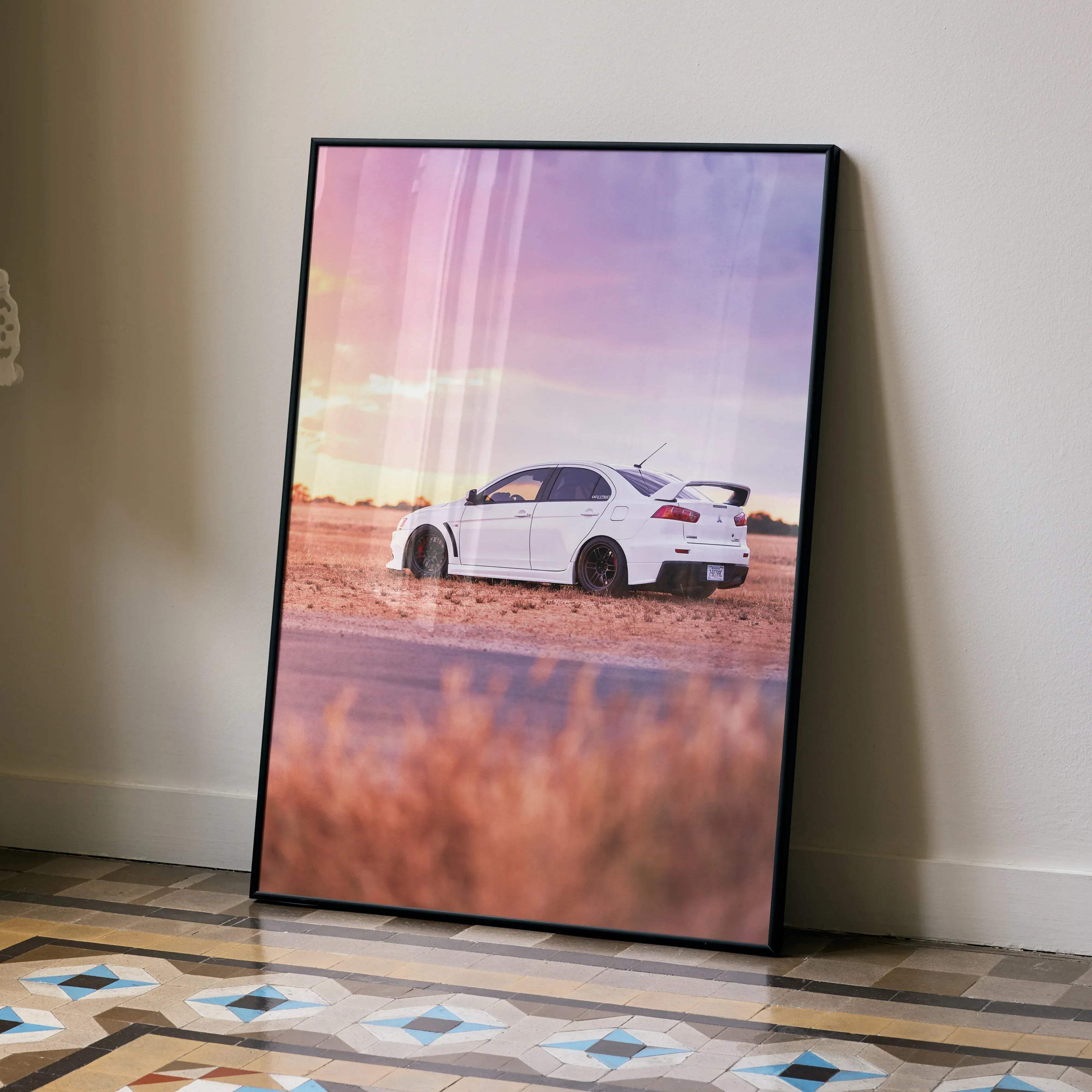 A framed poster of a white Mitsubishi Lancer Evolution sports car in a field at sunset printed on matte paper