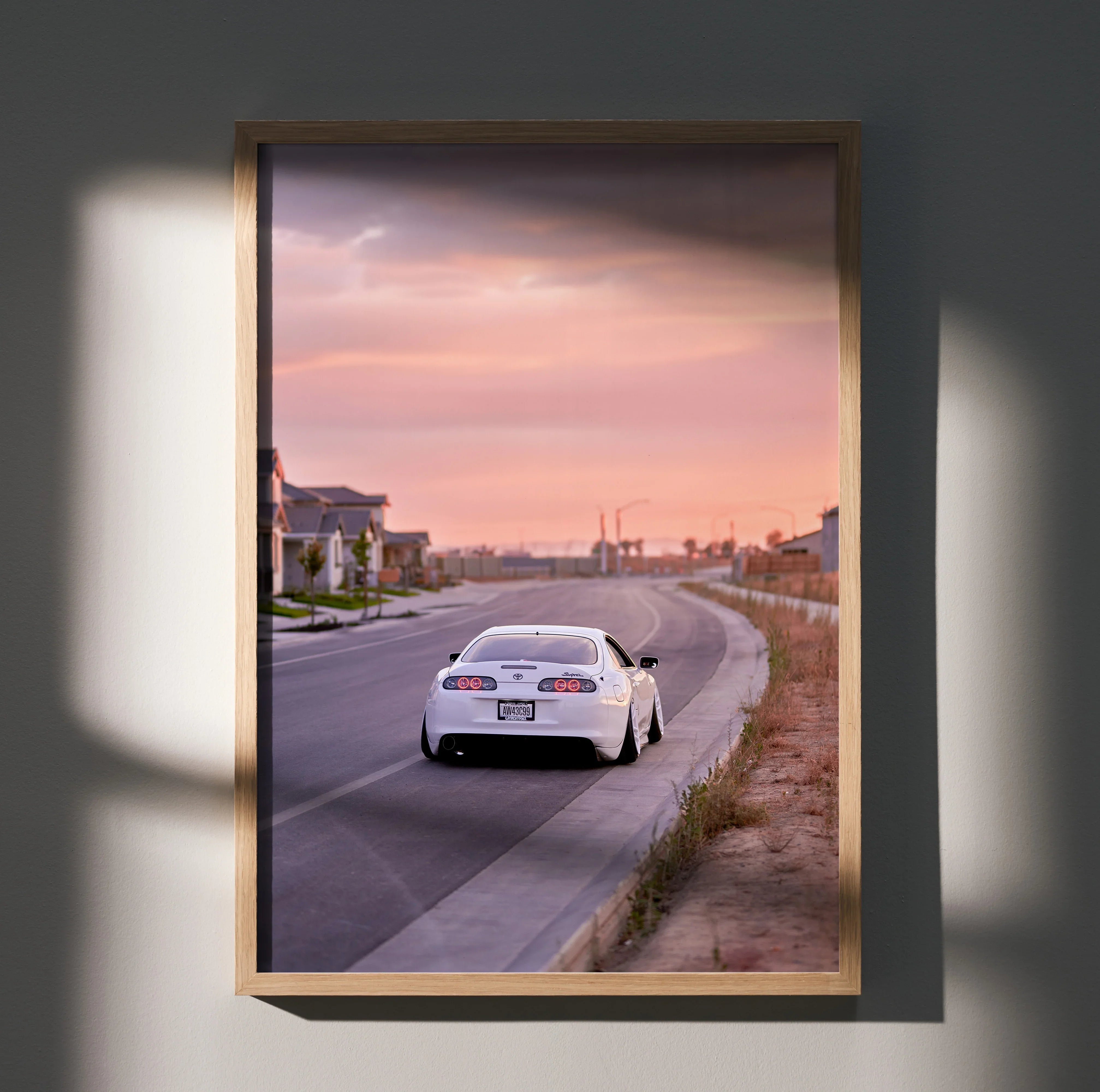 Supra MK4 sports car driving on suburban road at sunset poster wall art in wooden frame.