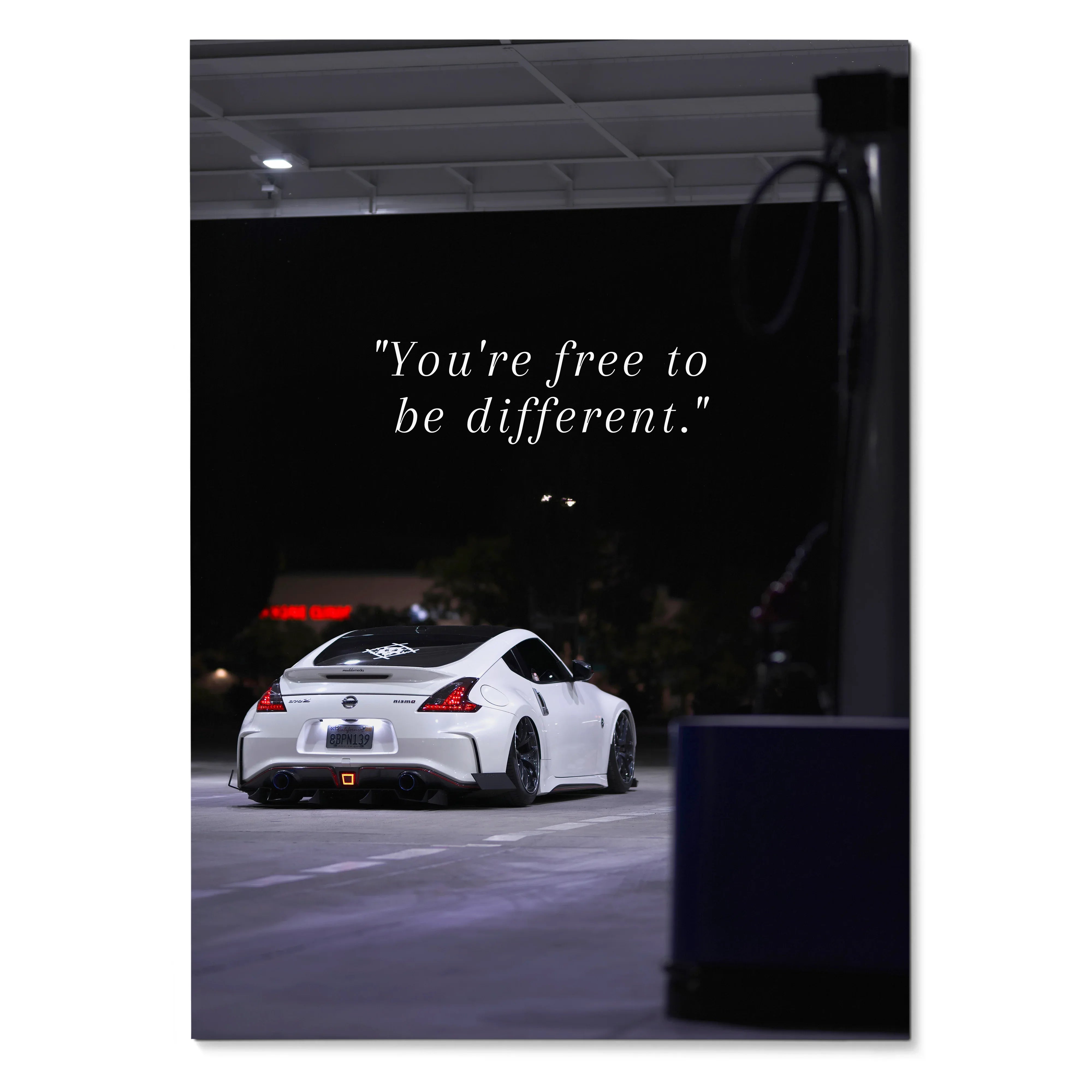 White Nissan 370z parked under streetlights with inspirational quote on black poster wall art.