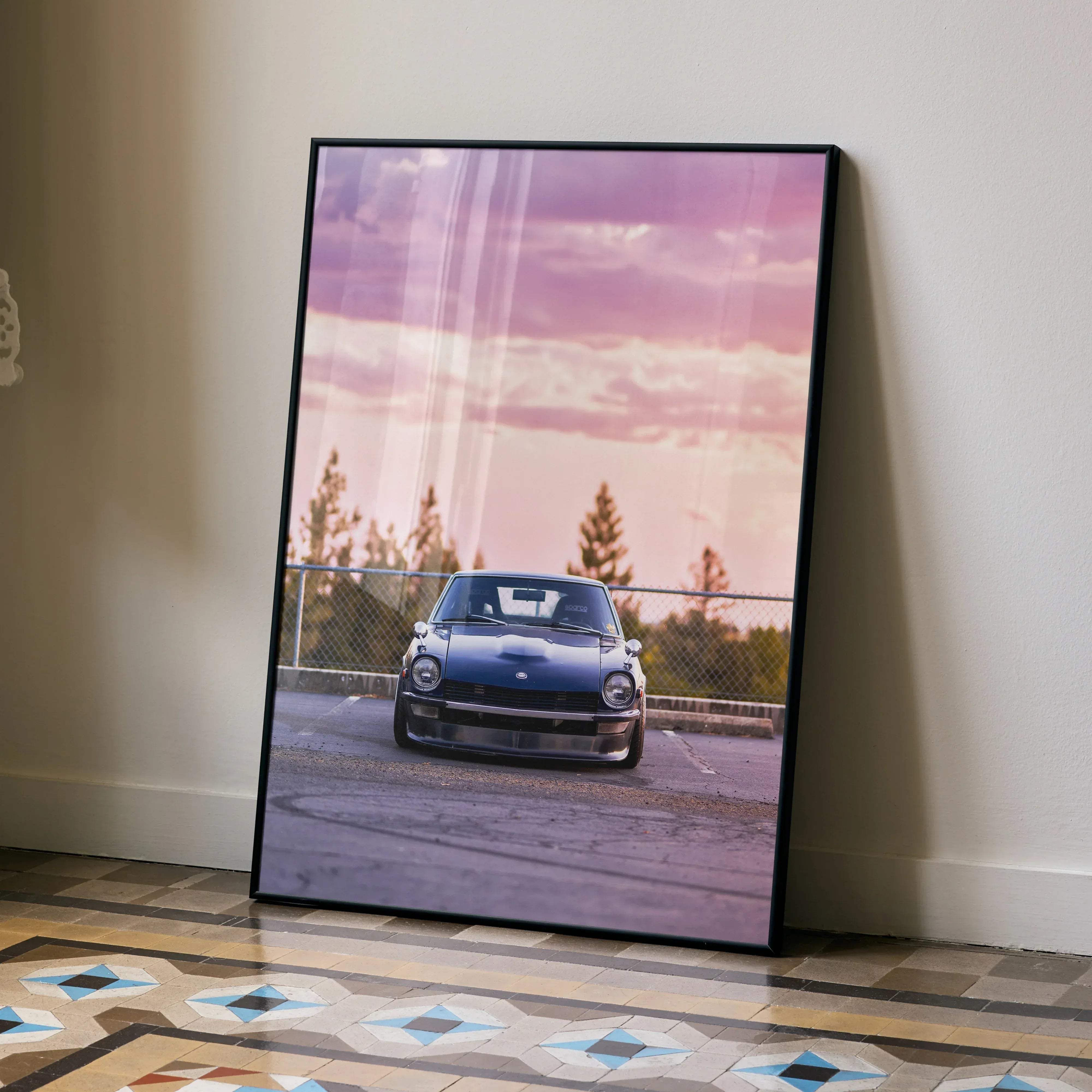 A framed poster of a blue Nissan 240z classic sports car under a pink and purple sky in a black frame
