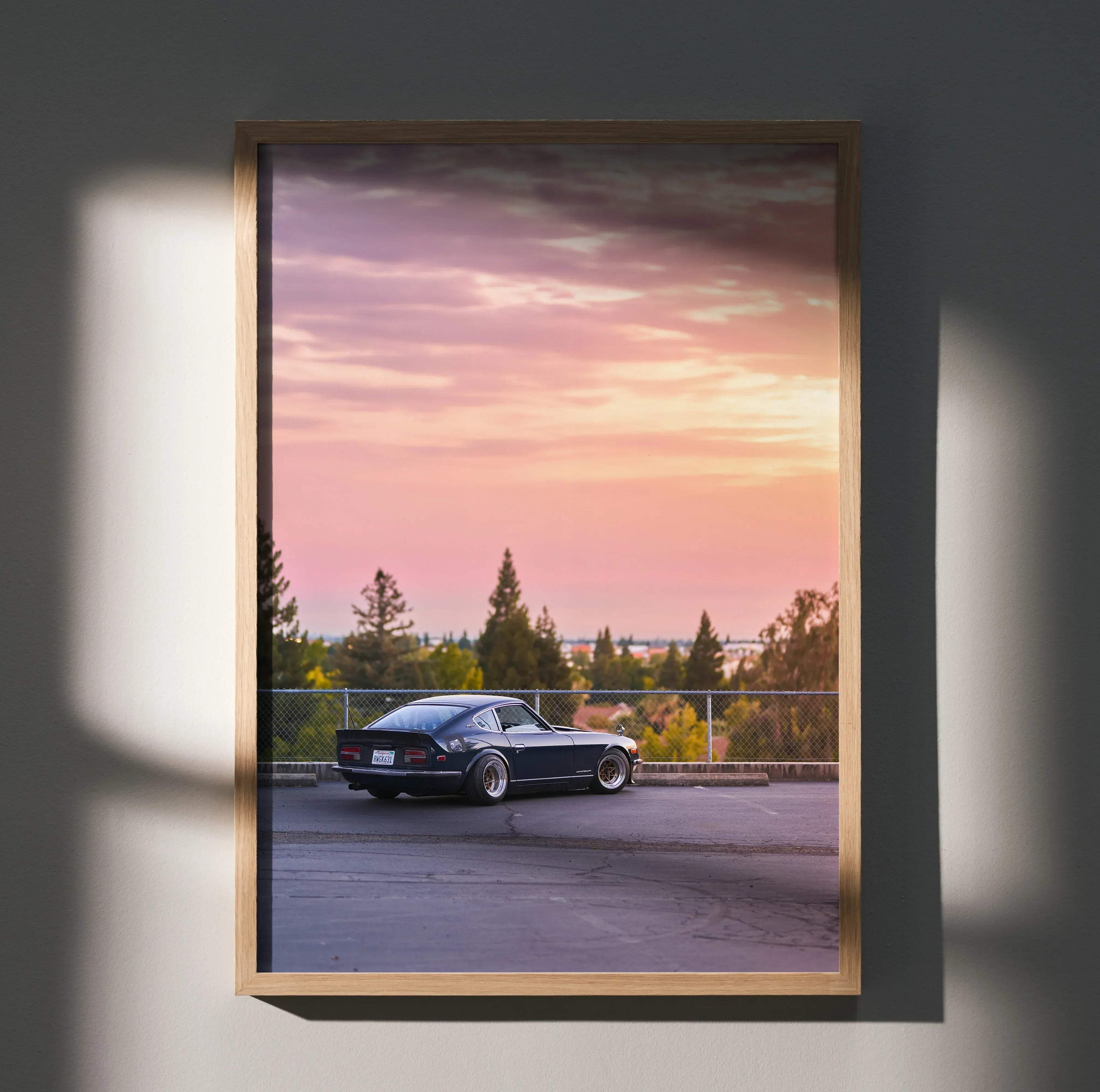 A framed high resolution poster of a dark blue nissan 240z classic sports car parked under a colorful sunset sky