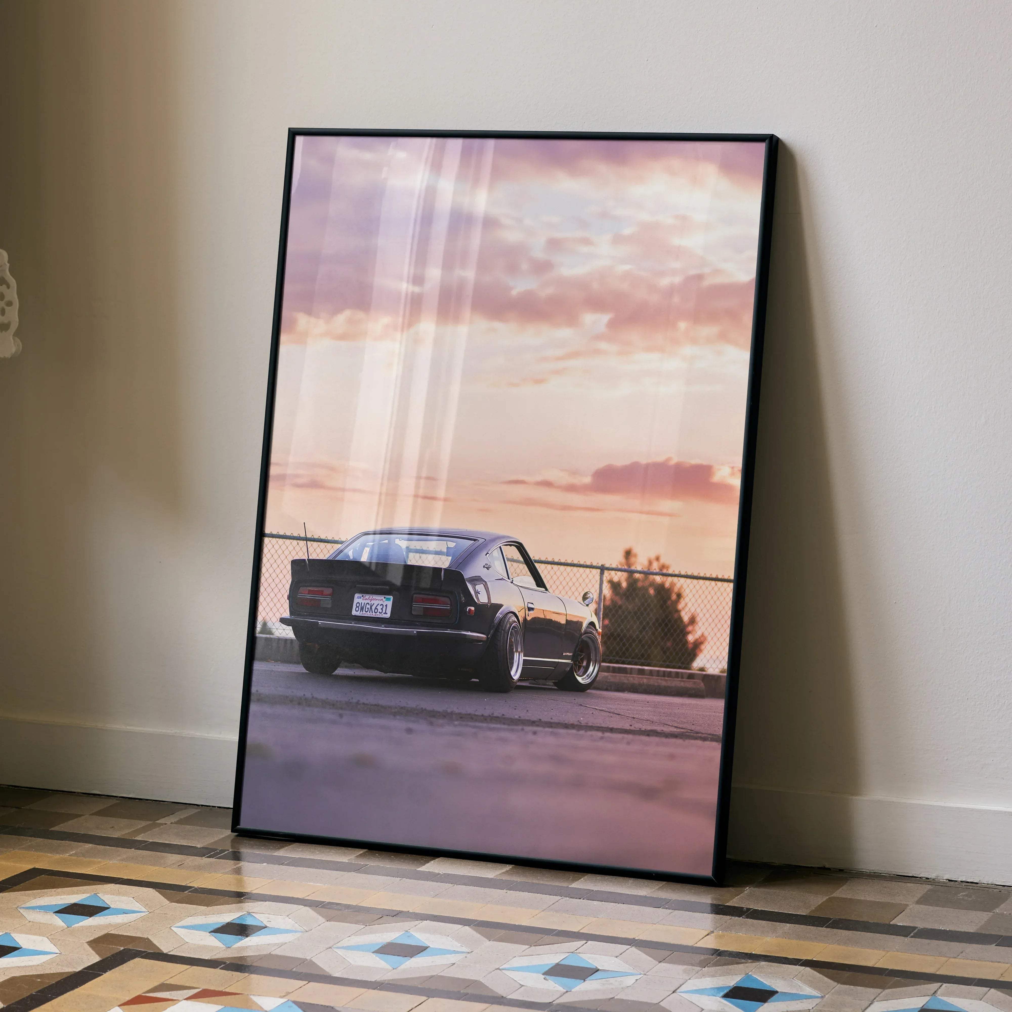 Black framed poster of a sleek dark-colored nissan 240z classic sports car at sunset against a pink purple sky