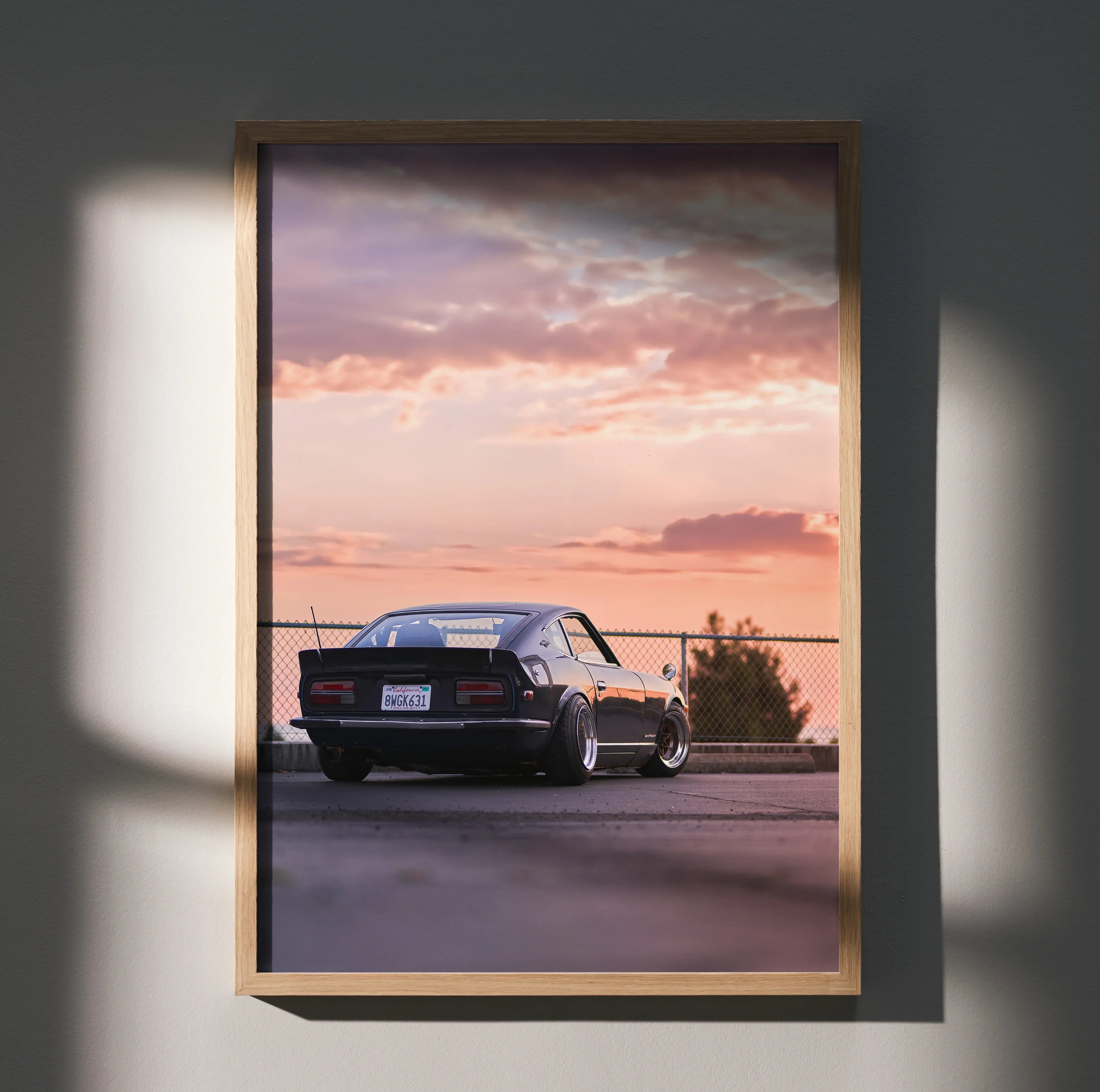 Nissan 240z poster wall art featuring a black car at sunset with pink and purple clouds.