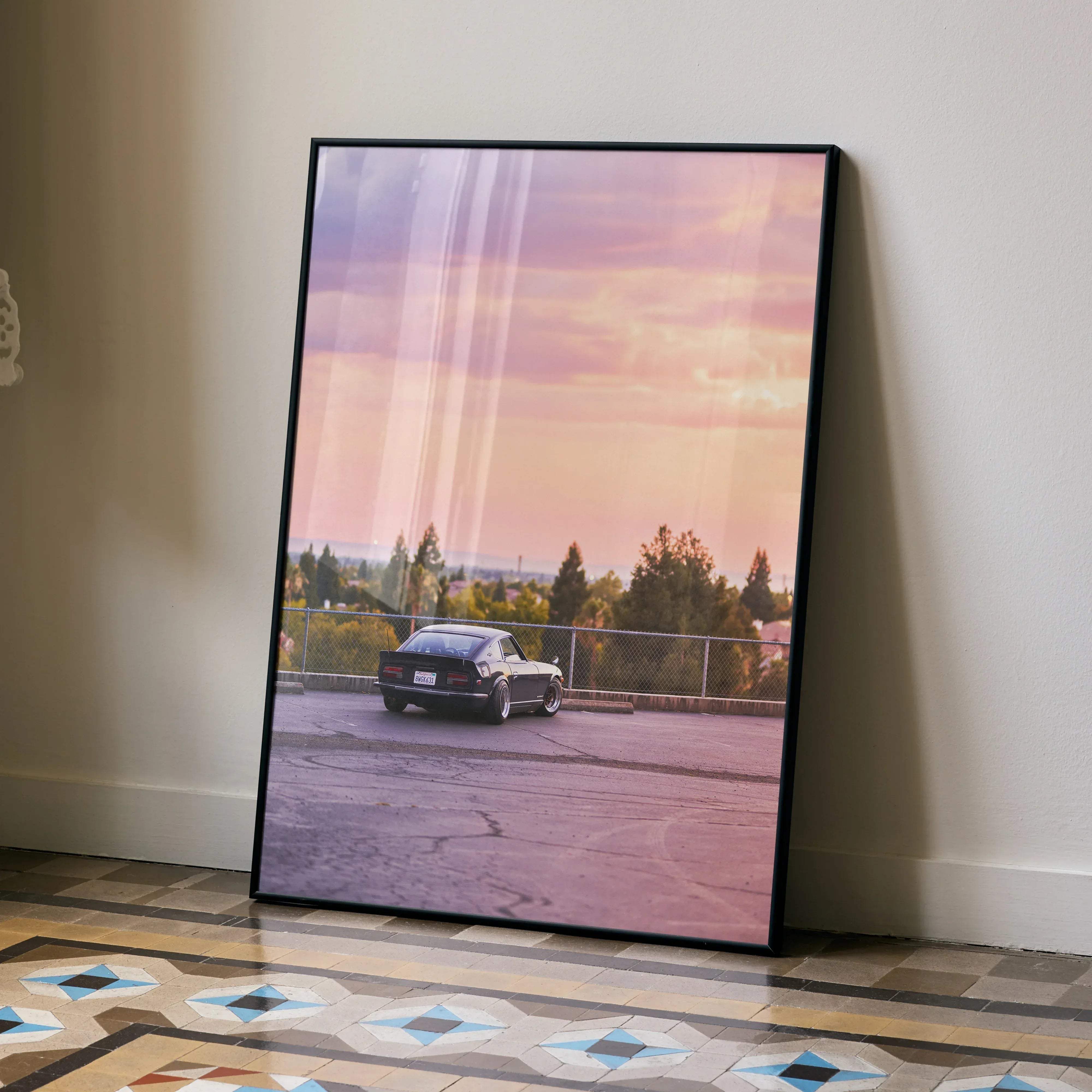 Black-framed art print of a black nissan 240z sports car parked on asphalt under a pink purple sunset sky