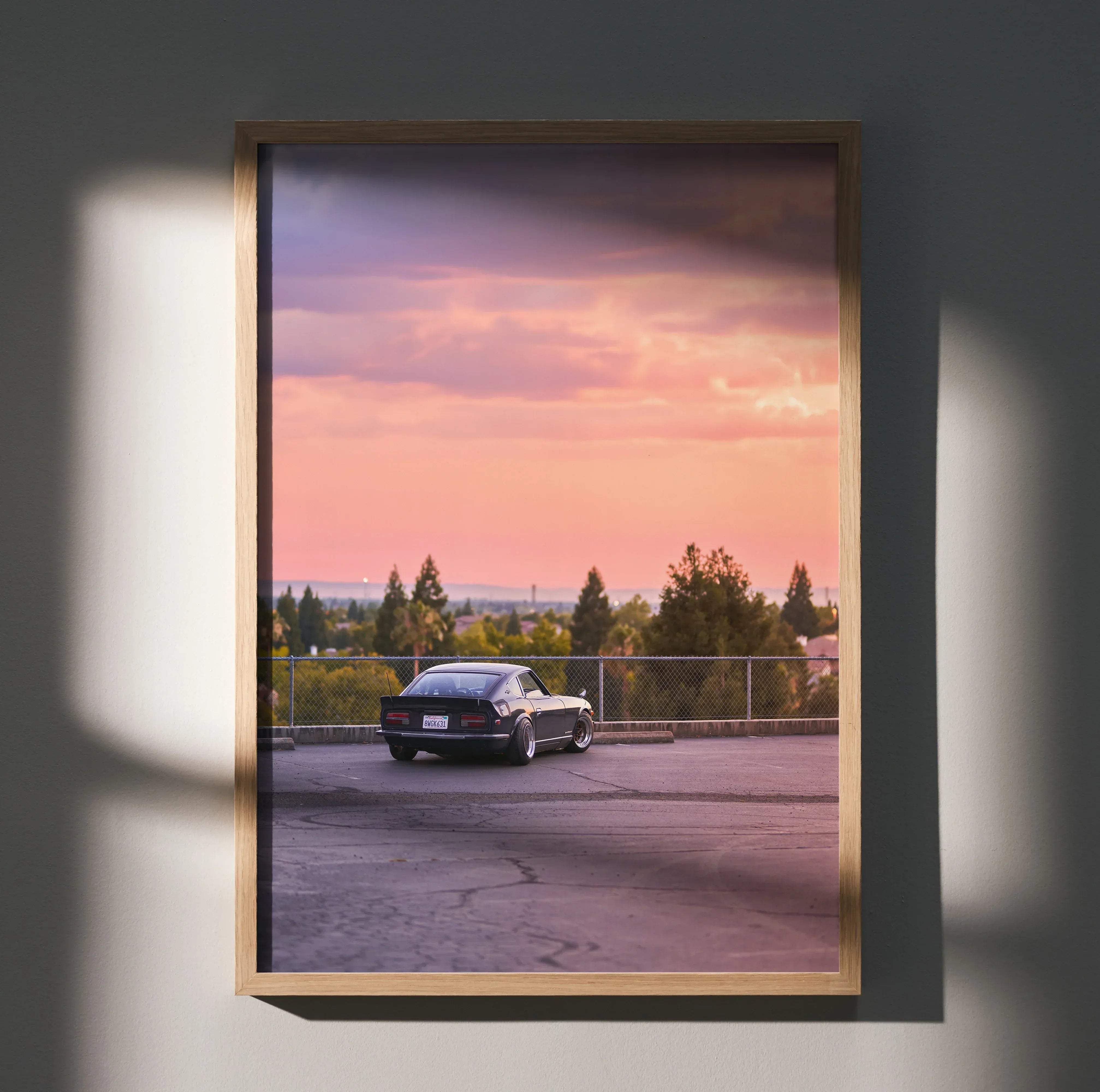 A framed high resolution poster of a black classic nissan 240z car parked under a pink and purple sunset sky