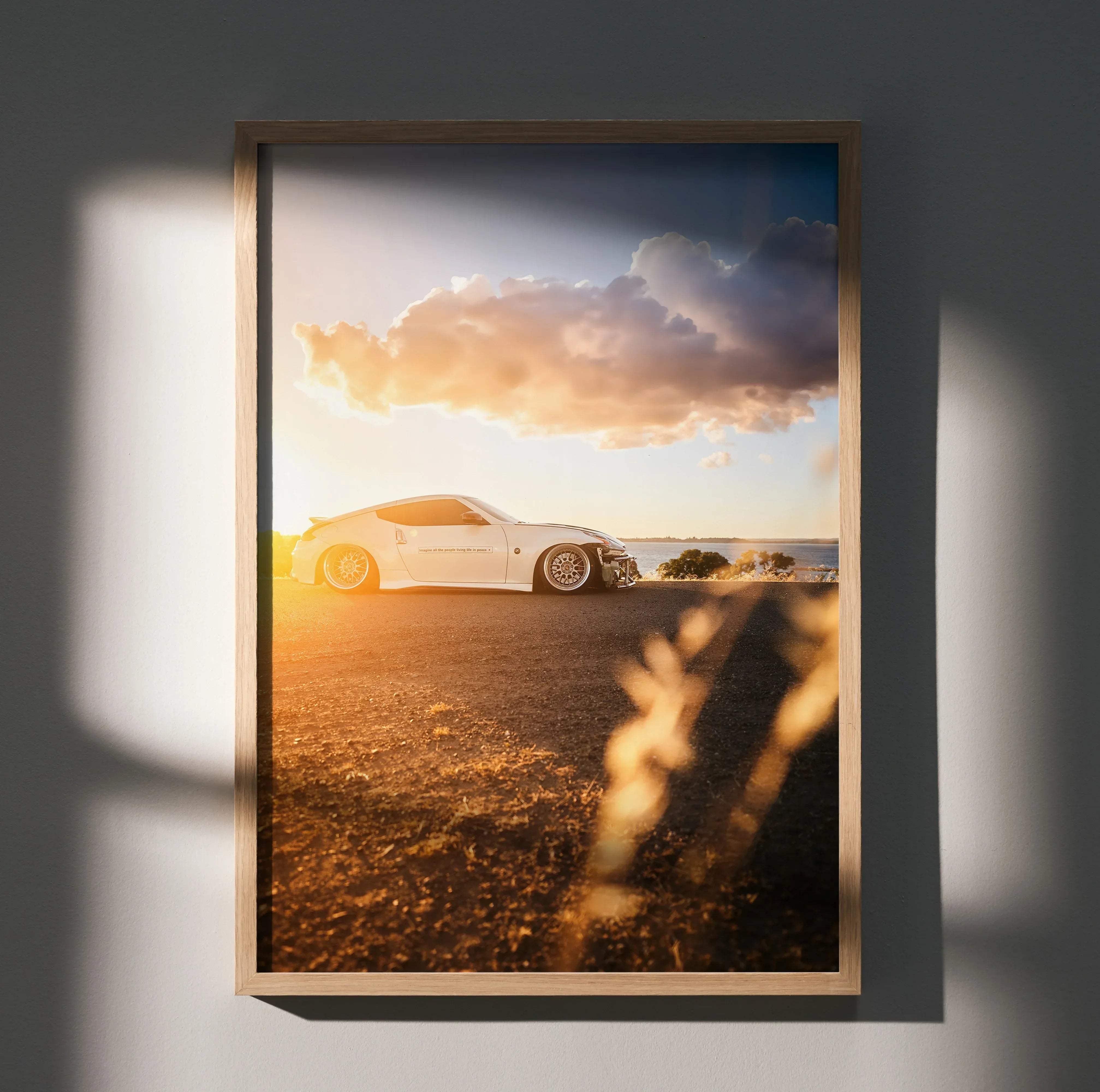 A framed high resolution poster of a white nissan 370z sports car parked on a sunlit beach under dramatic clouds