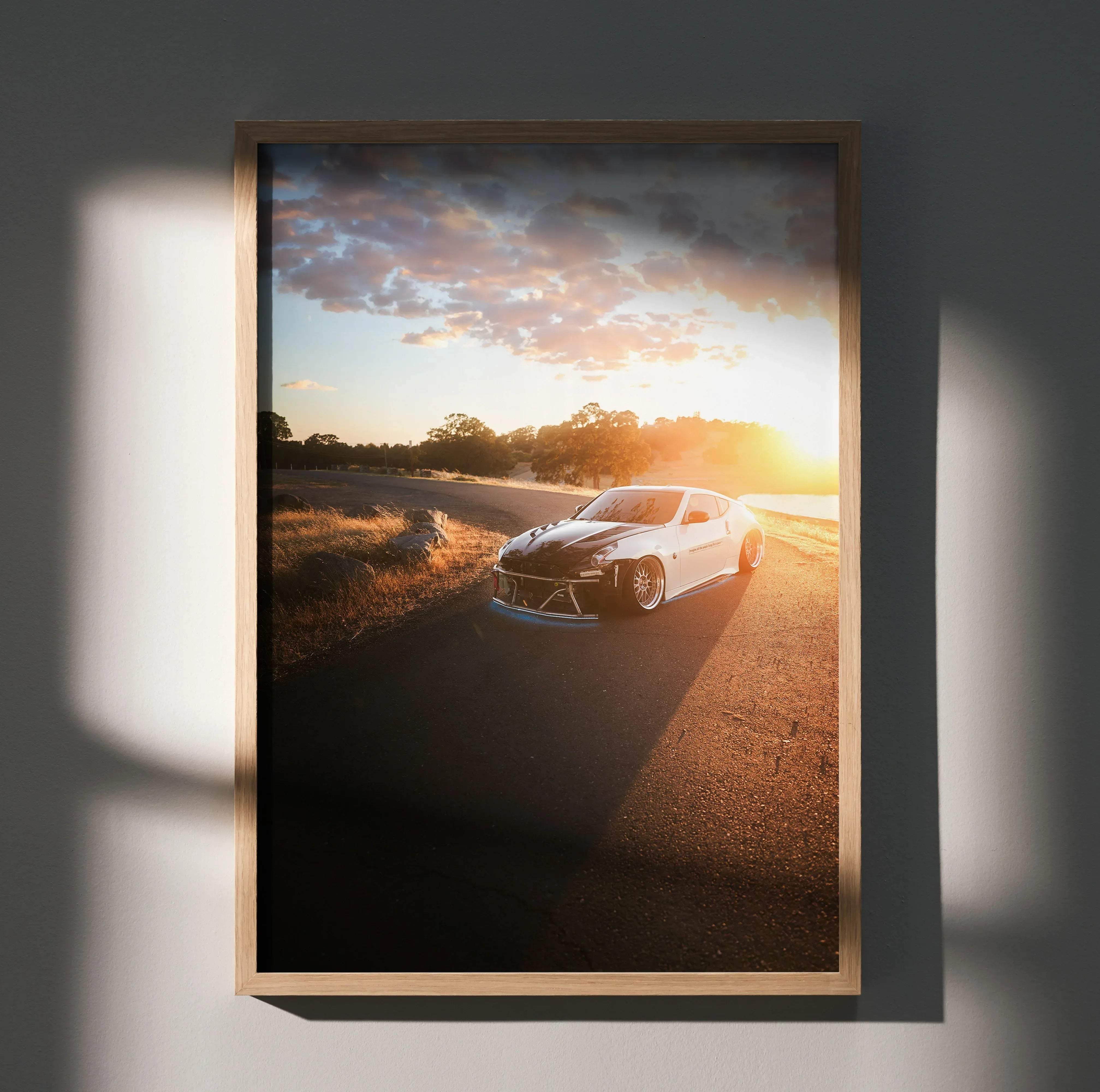 A framed photograph of a white Nissan 370z sports car with black accents at sunset on an asphalt road poster