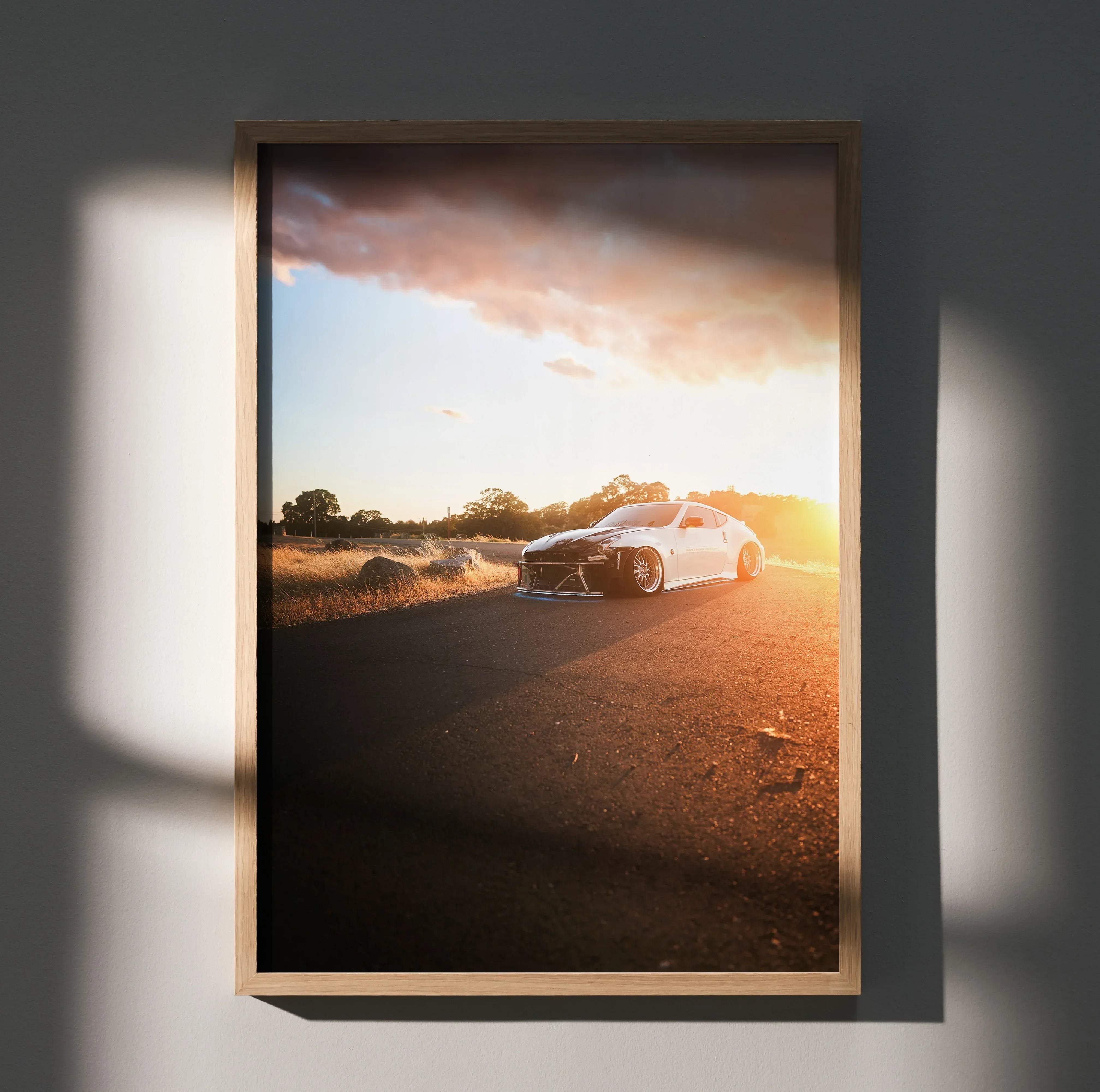 A framed high resolution photo poster of a white Nissan 370z drifting on a sunlit road with dramatic clouds