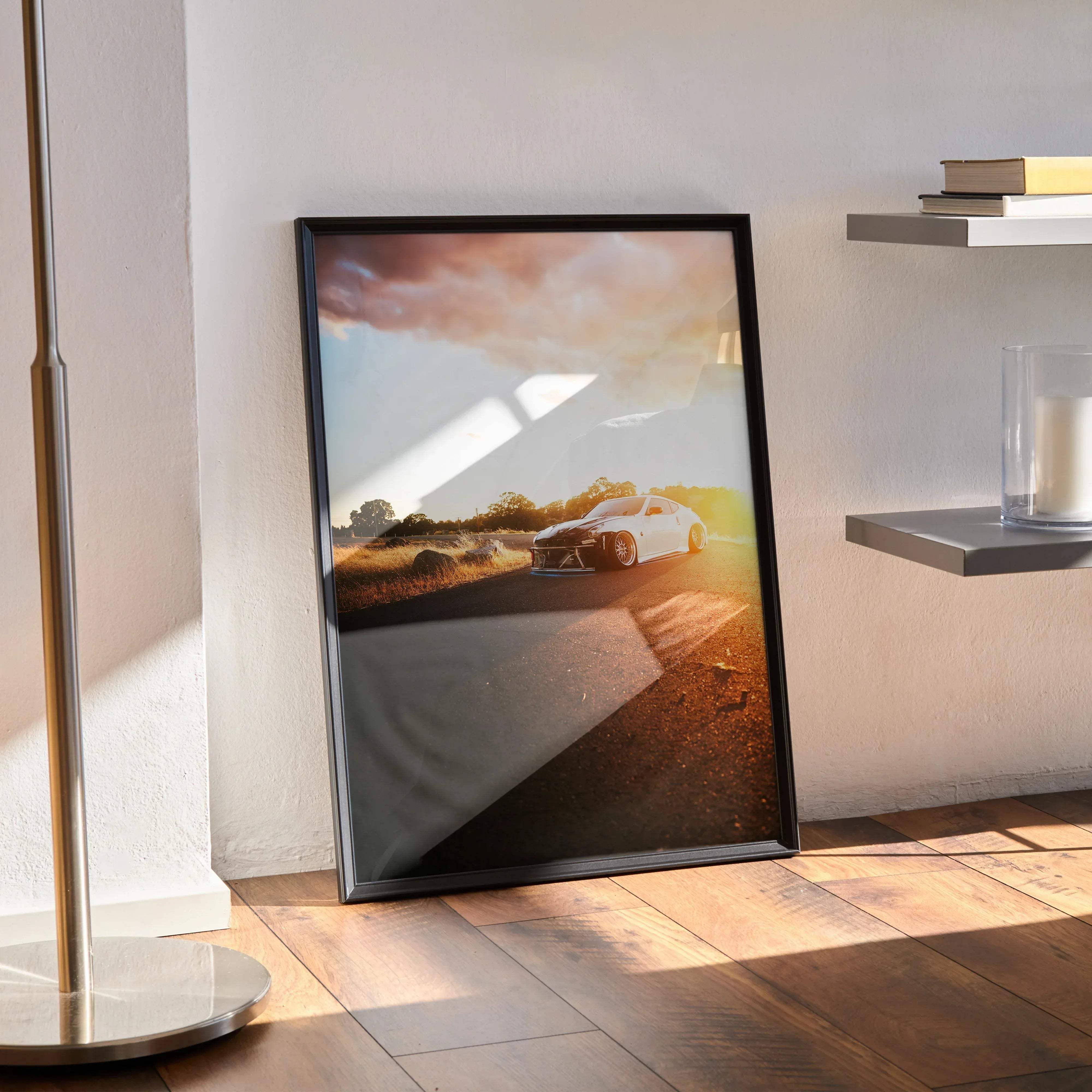 Black-framed poster of a white nissan 370z sports car on a sunlit road under dramatic clouds