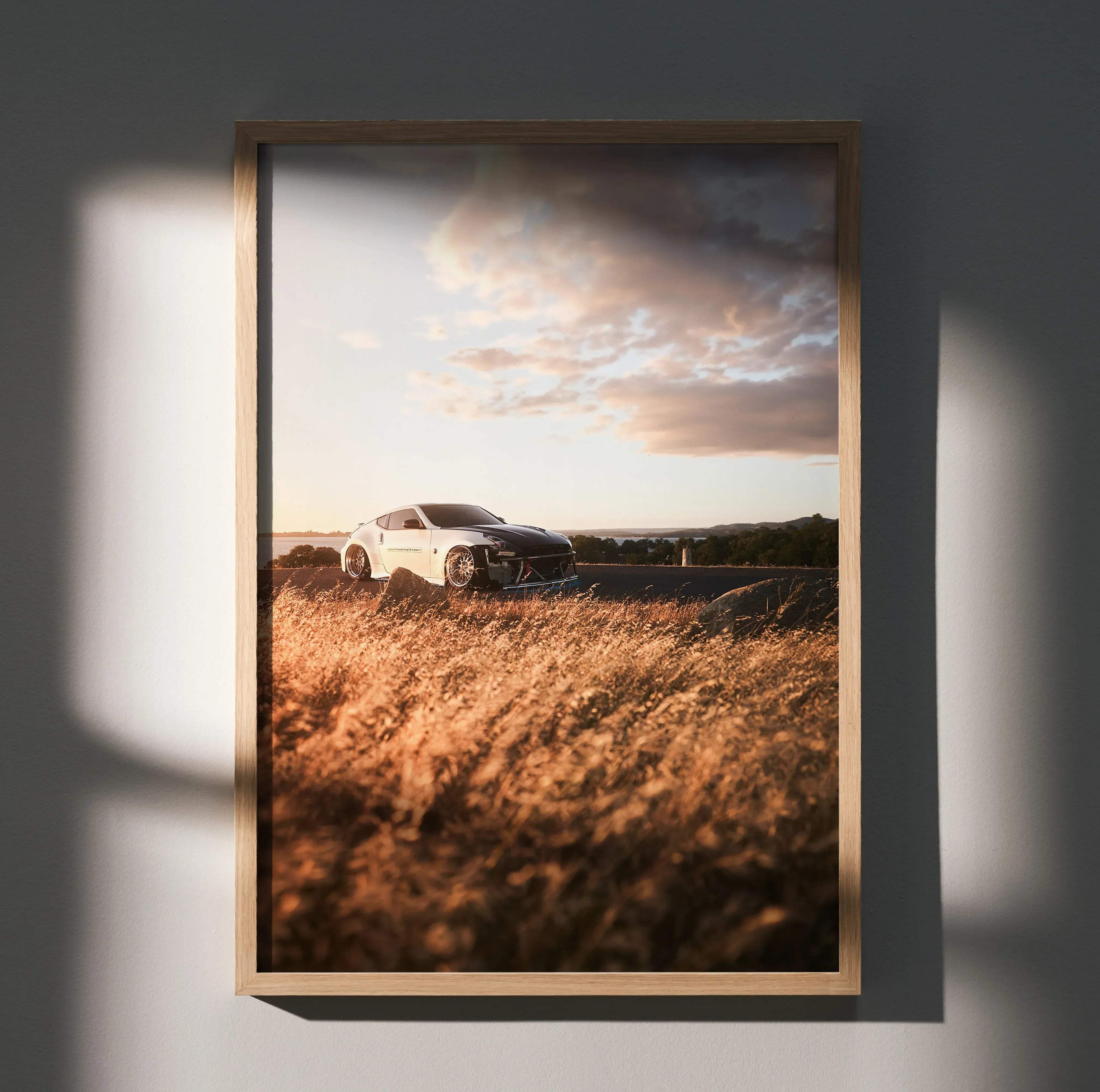 A framed high resolution poster of a white Nissan 370z sports car parked in golden grass under dramatic sky