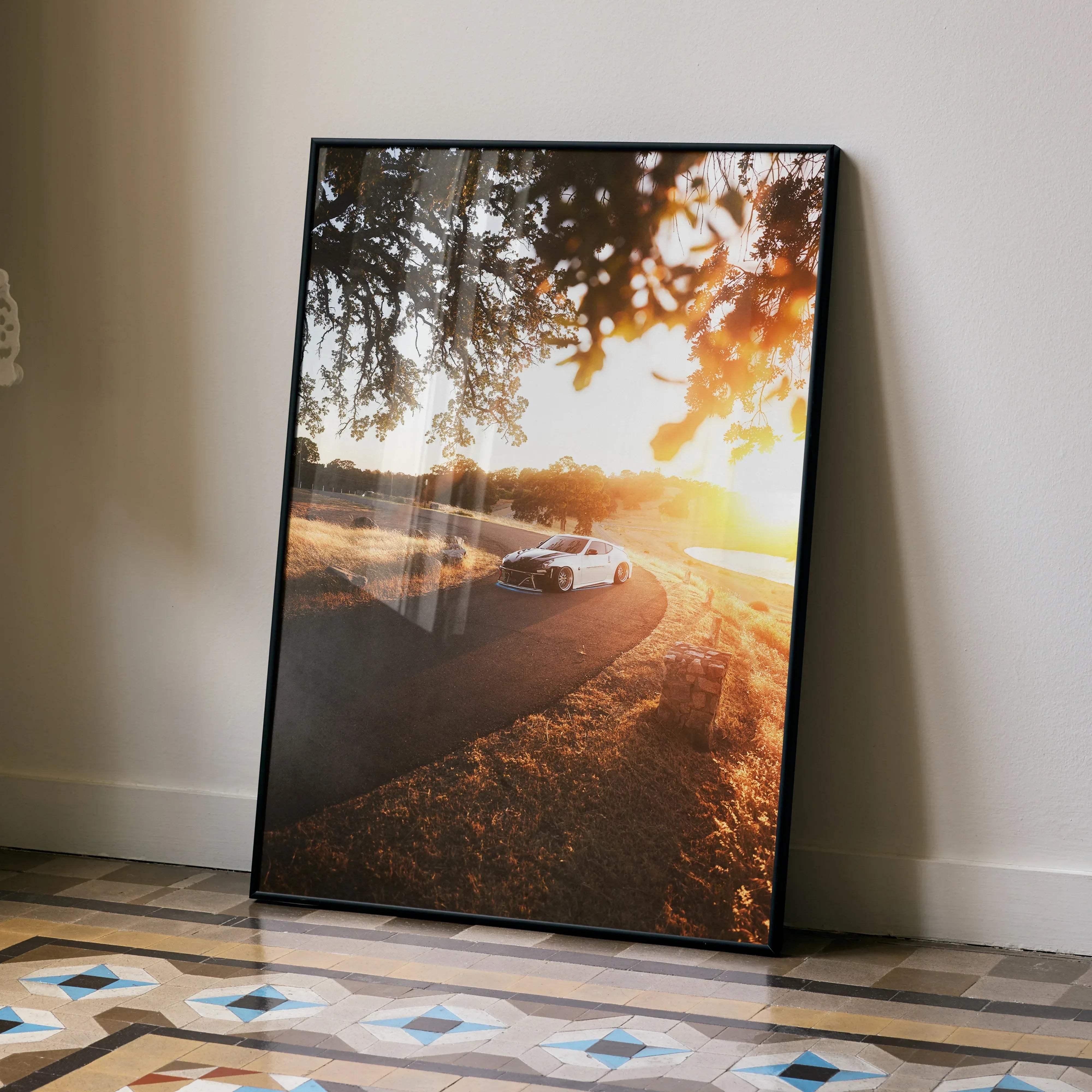 Black-framed canvas print of white nissan 370z driving along sunlit country road under tree branches