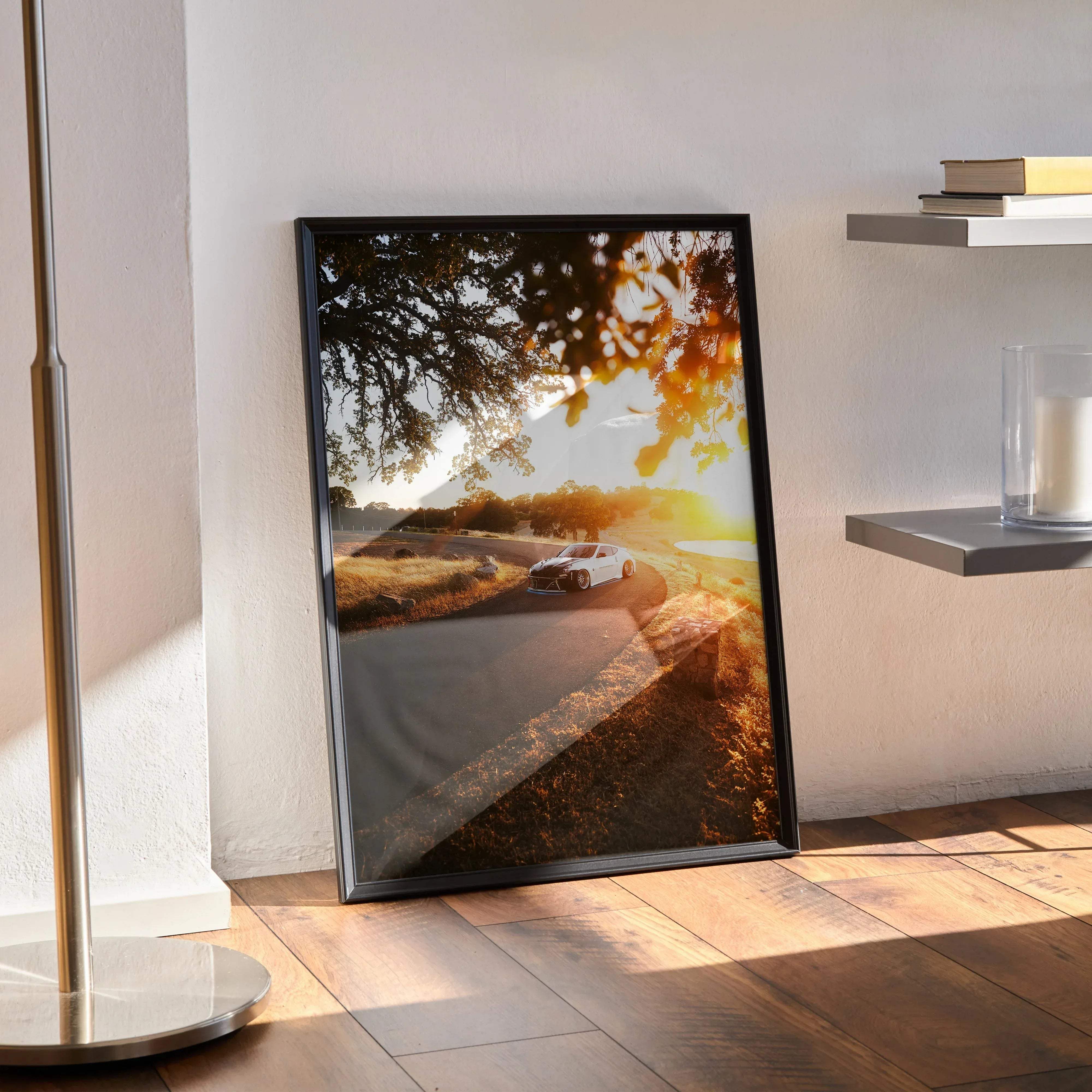 Black-framed wall art poster featuring a white Nissan 370z sports car driving on a sunlit road under golden trees