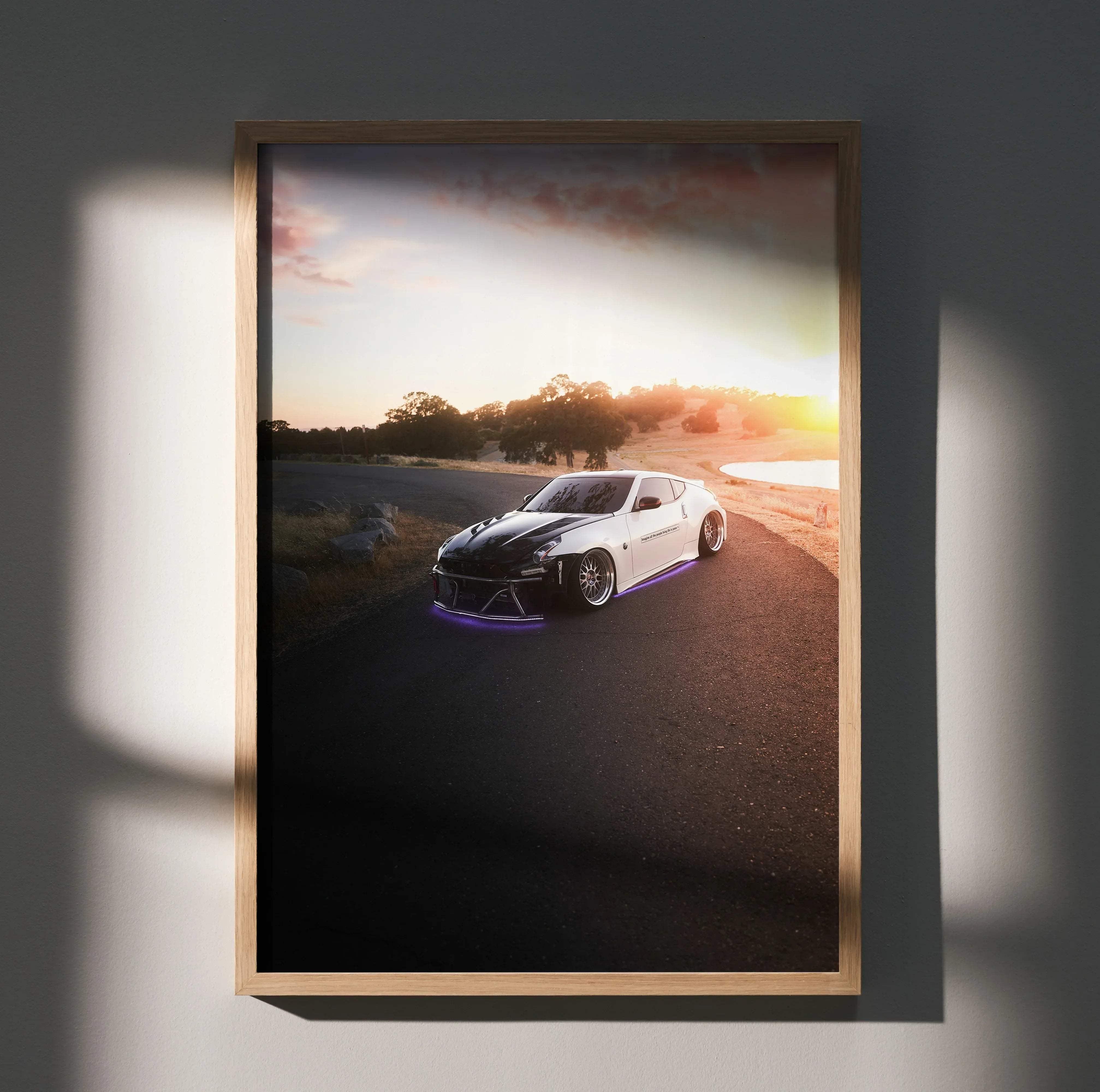 A framed poster of a white and black Nissan Z sports car with purple underglow lighting at sunset on a road