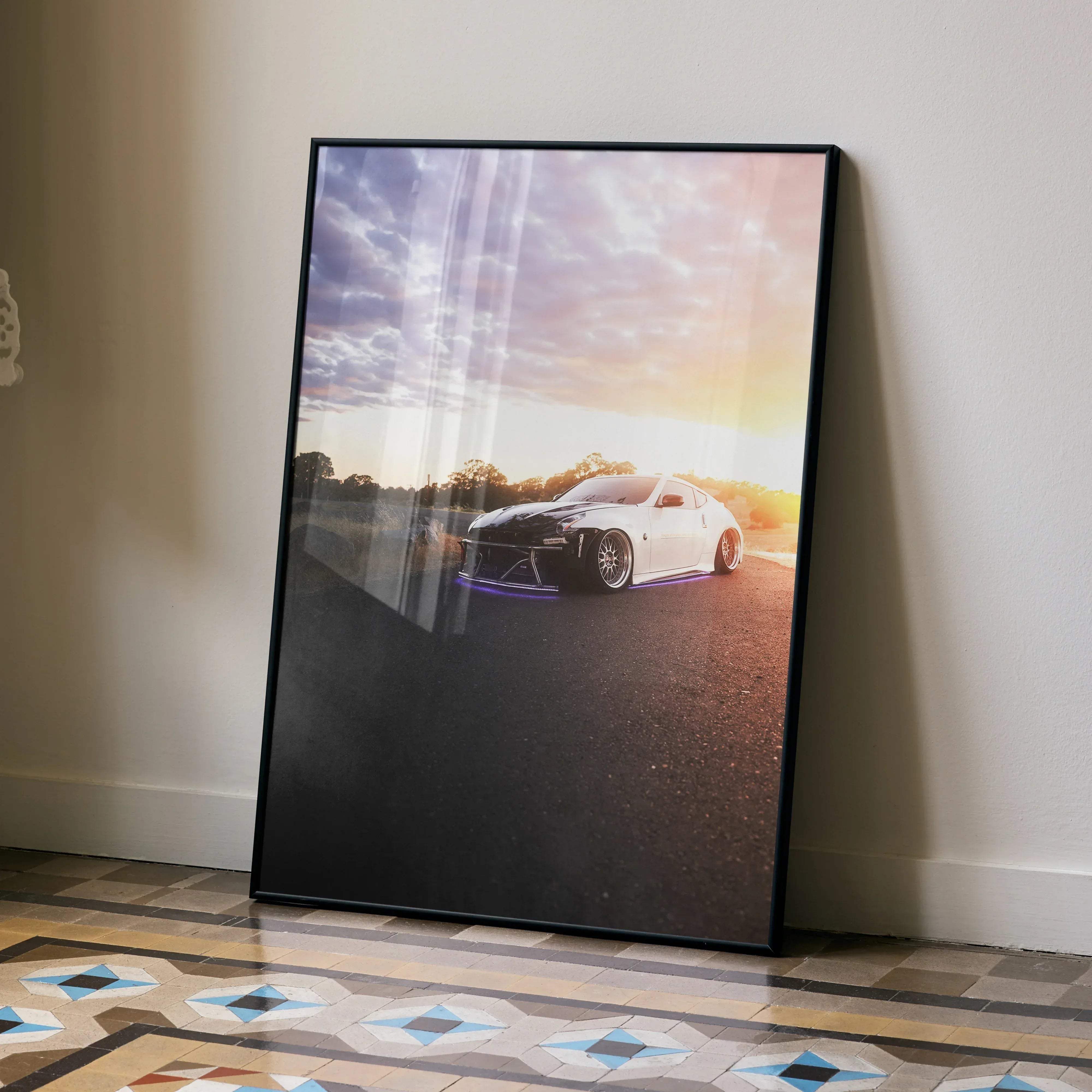 Black-framed poster of a white nissan 370z sports car with purple underglow parked on asphalt road at sunset