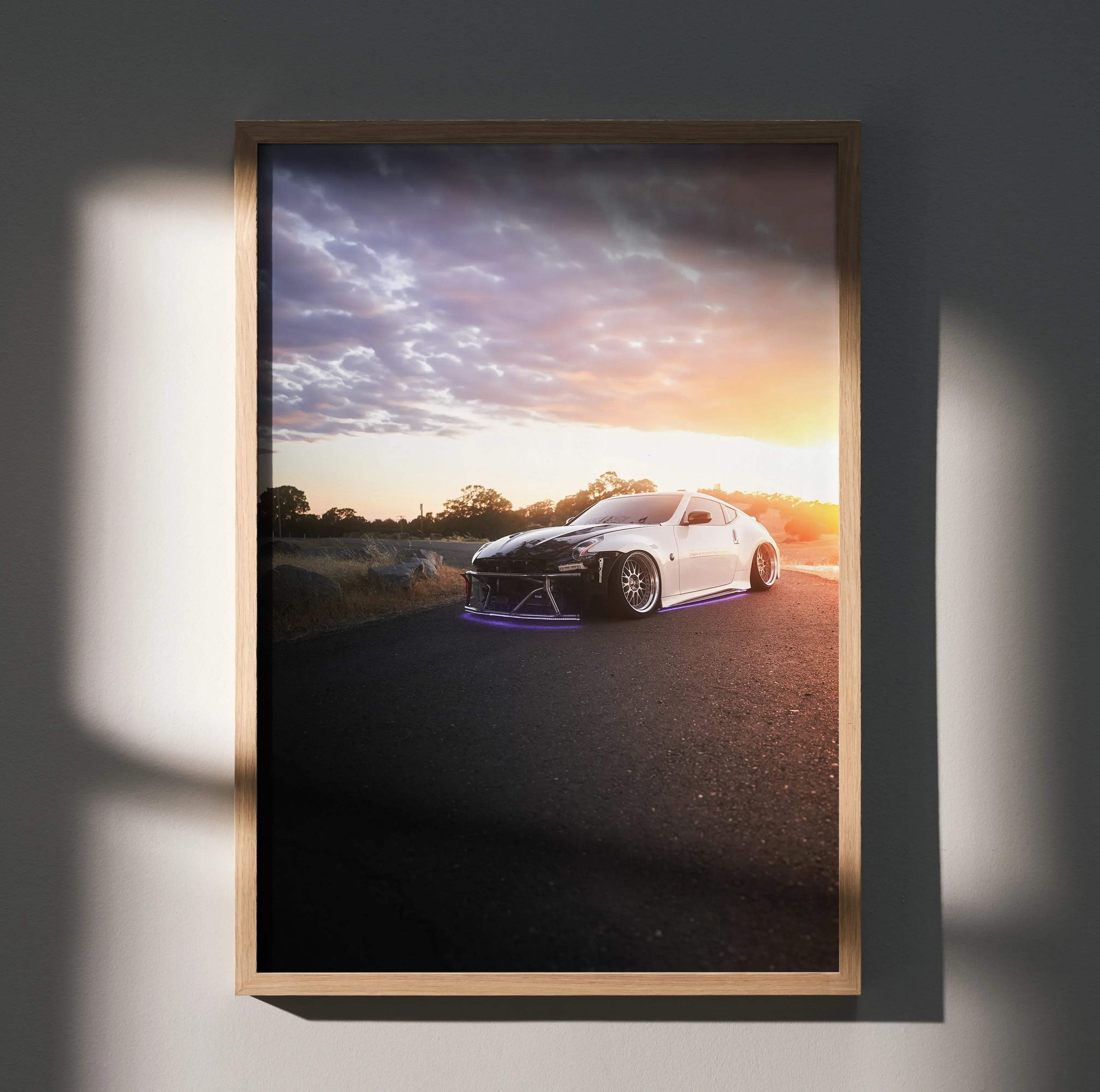 A framed poster of a white Nissan 370z sports car with black accents and purple underglow at sunset
