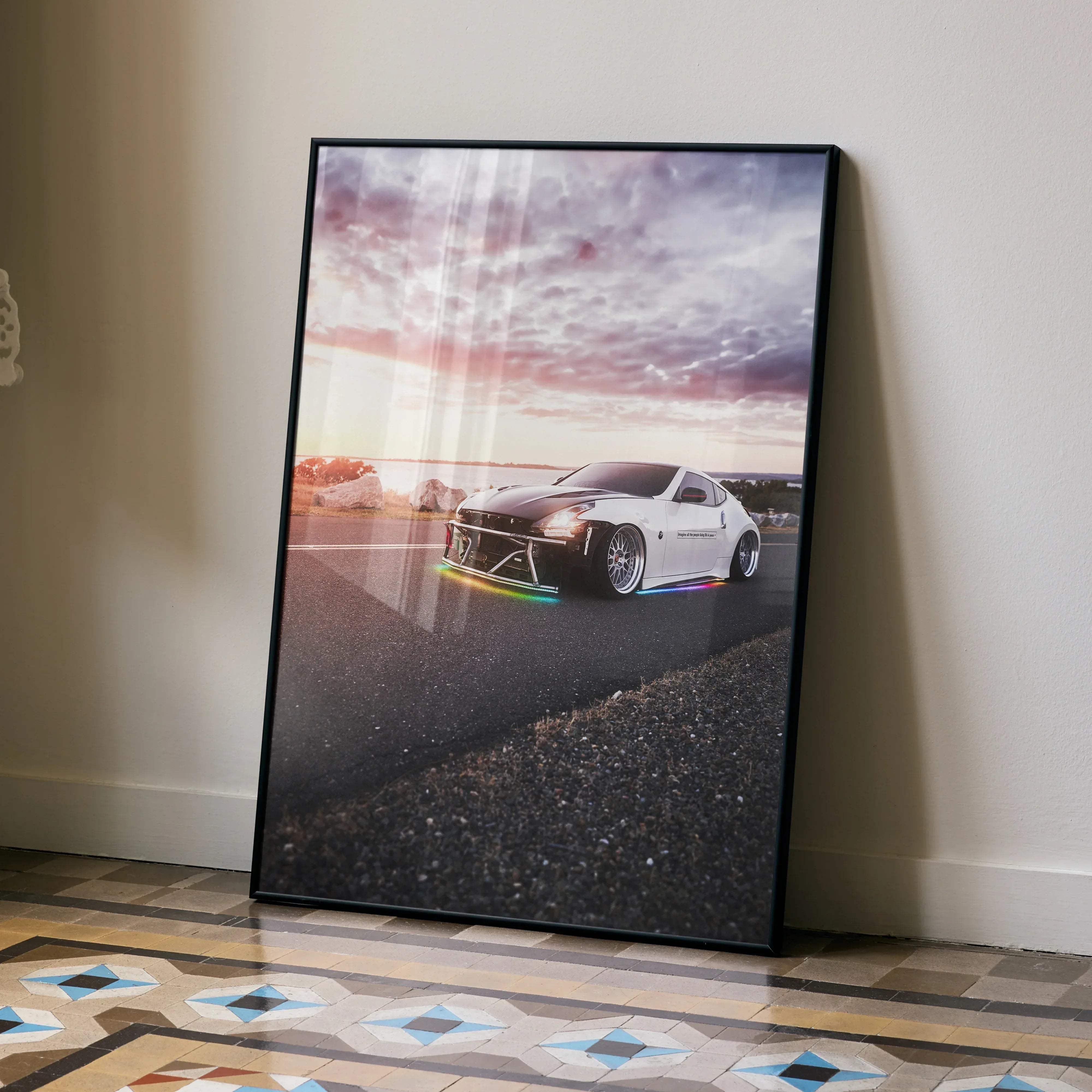 Black-framed poster of a white and black nissan 370z sports car with rainbow underglow lights at sunset