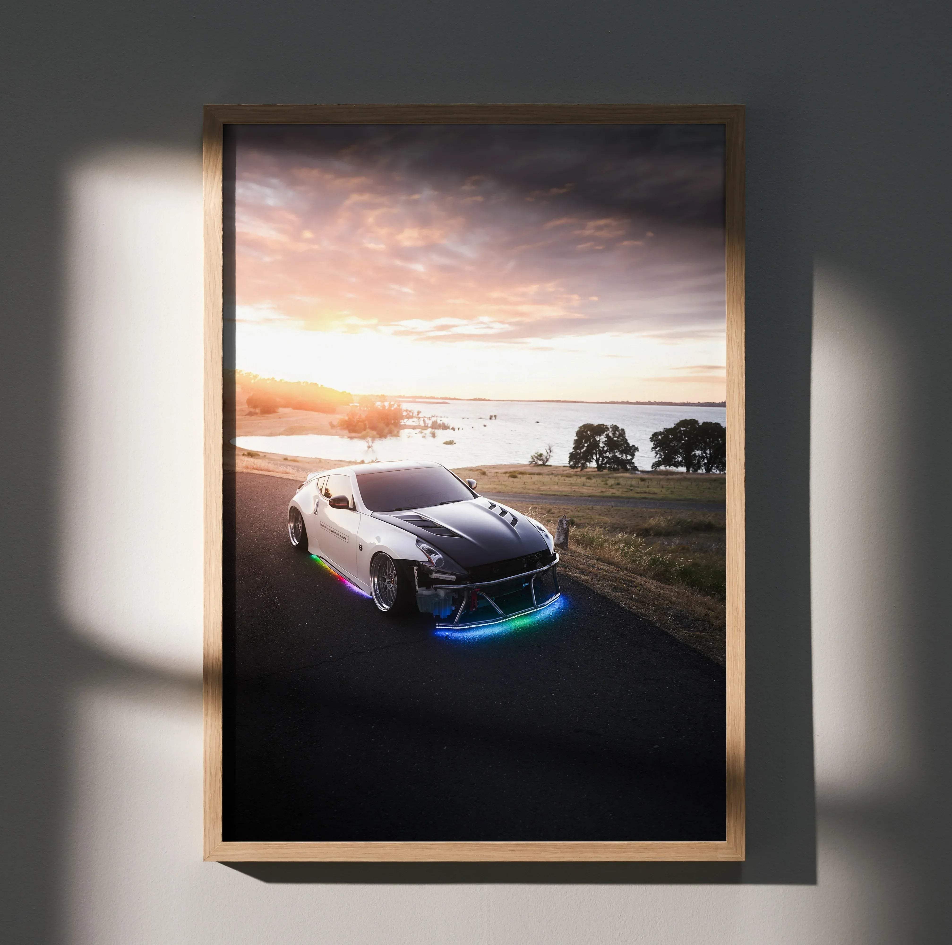A framed Nissan 370z car poster featuring a white and black sports car with glowing RGB underglow at sunset