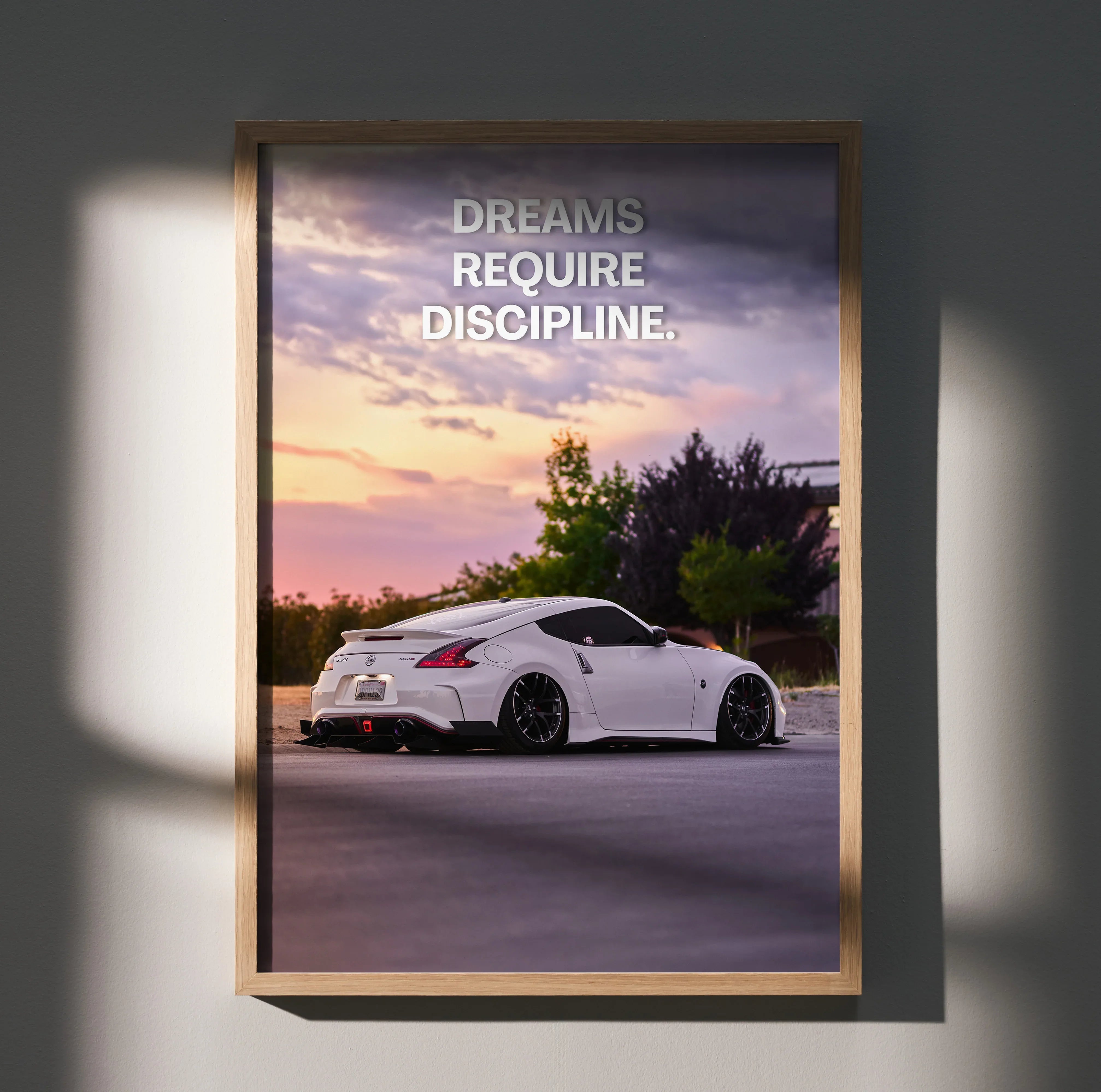 Motivational poster wall art featuring a white Nissan 370z at sunset with text "Dreams Require Discipline".