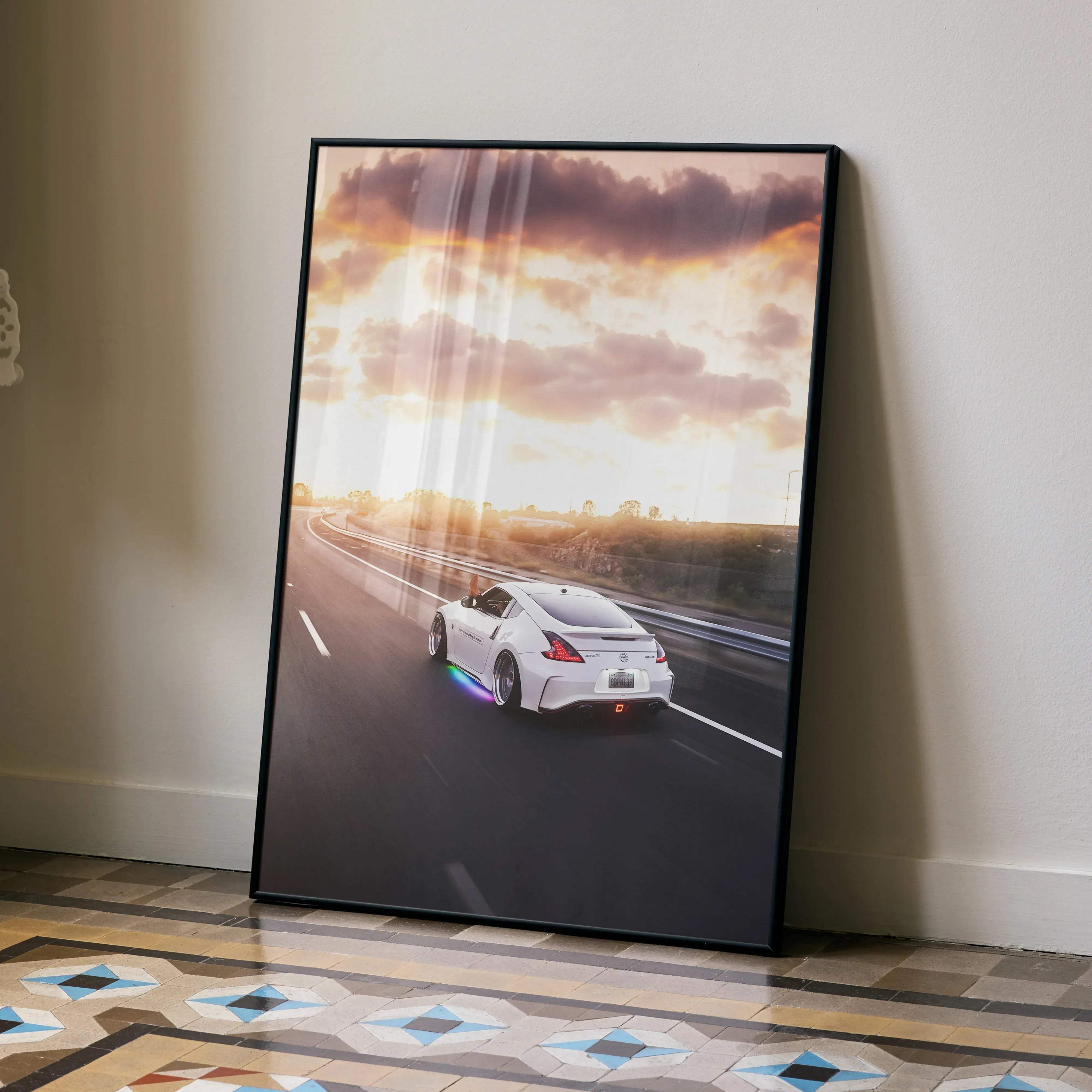 Black-framed poster of a white nissan 370z speeding at sunset with vibrant orange and purple clouds above