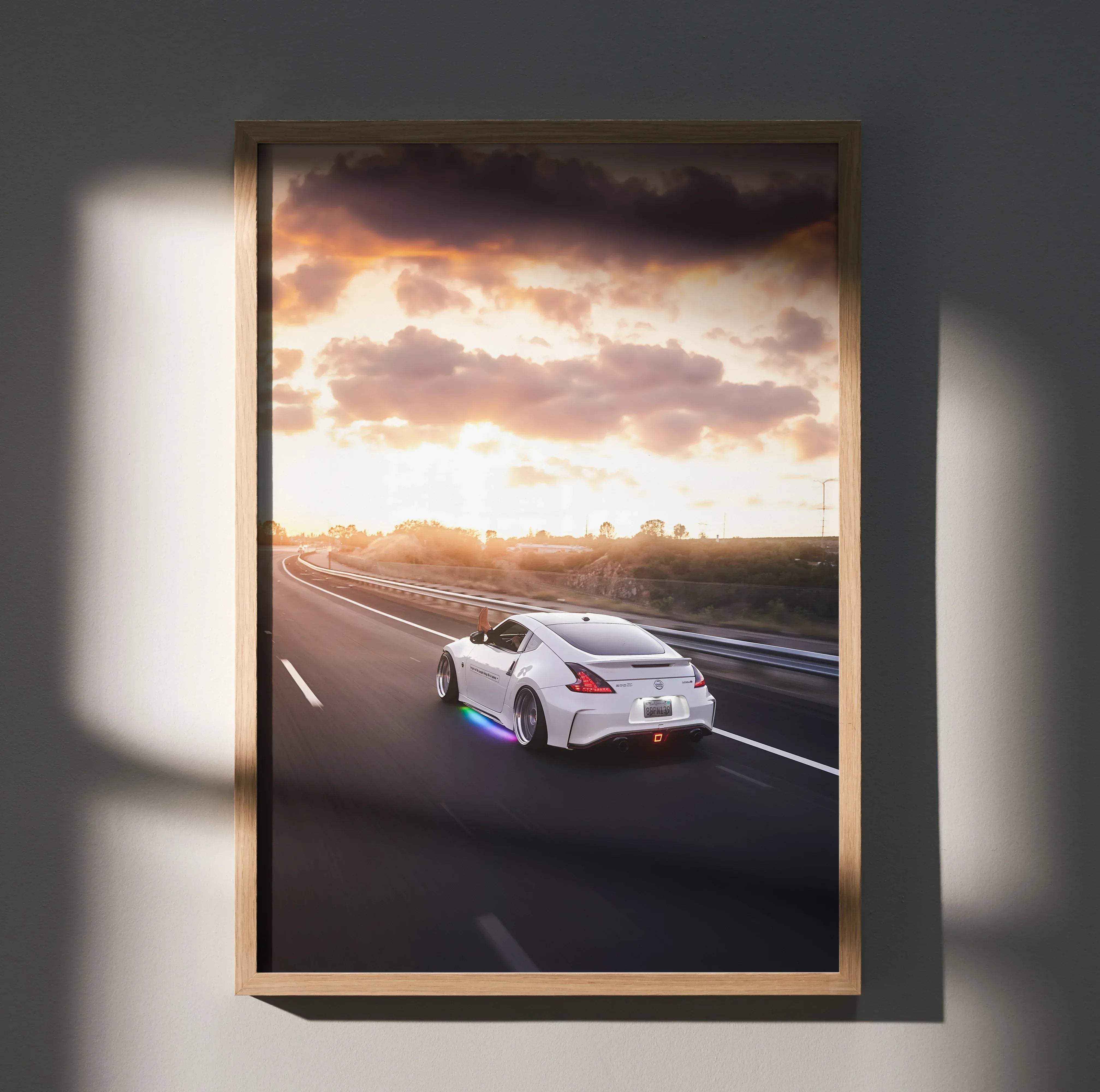 A framed high resolution poster of a white Nissan 370z sports car speeding on a highway at sunset with dramatic clouds
