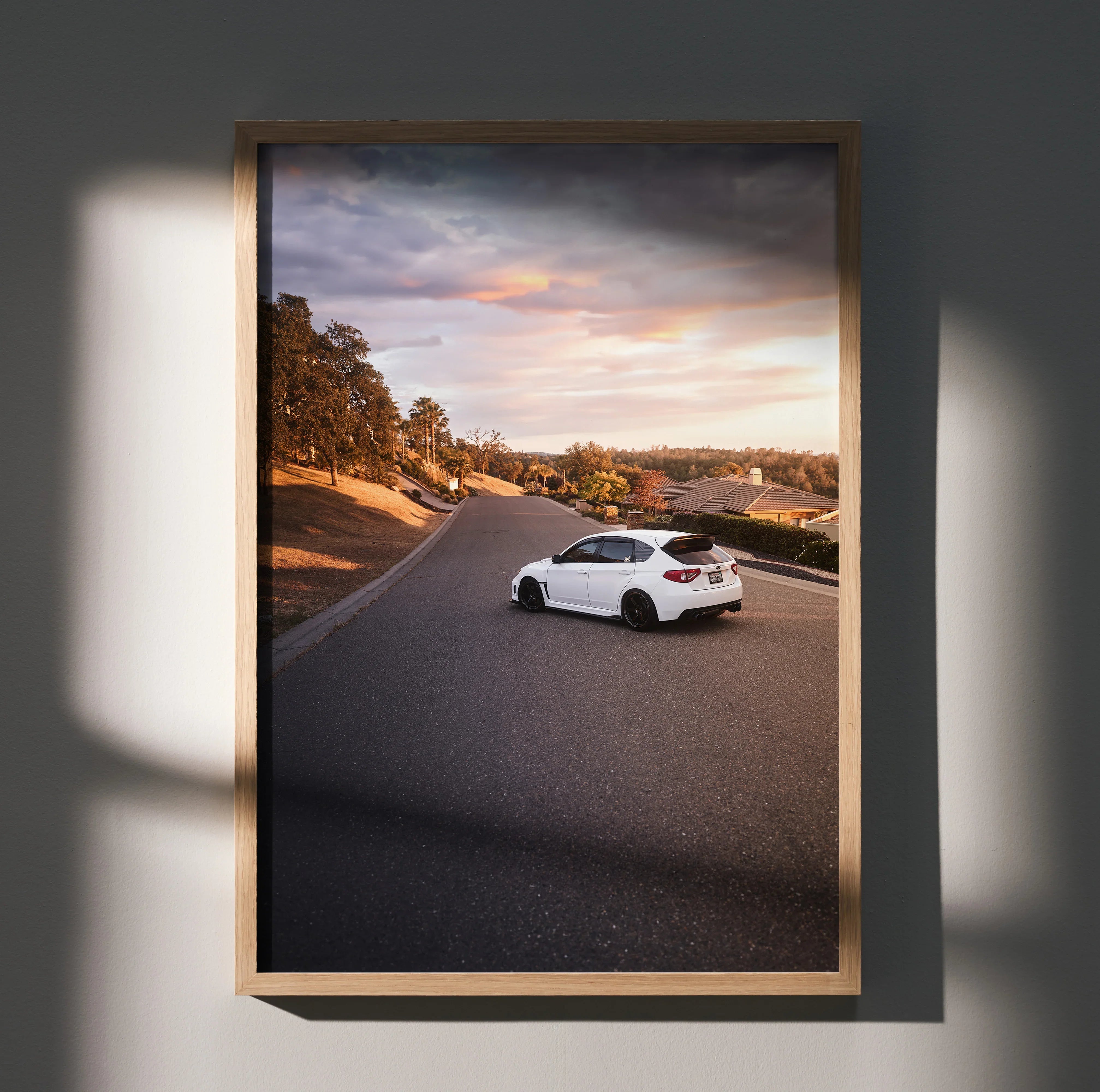 Subaru WRX STI driving on scenic road at sunset poster wall art in wooden frame.