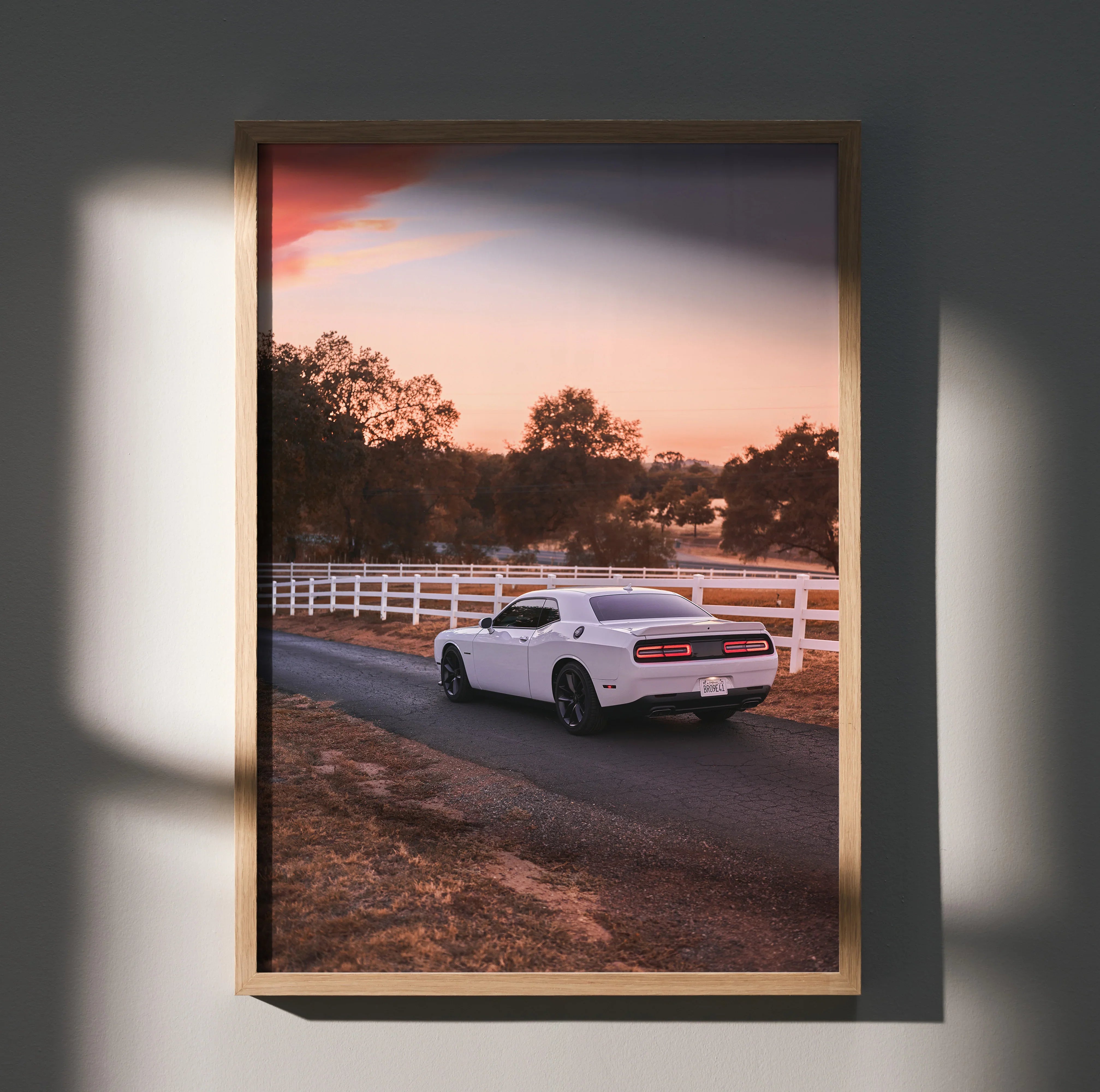 Dodge Challenger driving away on country road at sunset poster wall art in wooden frame.