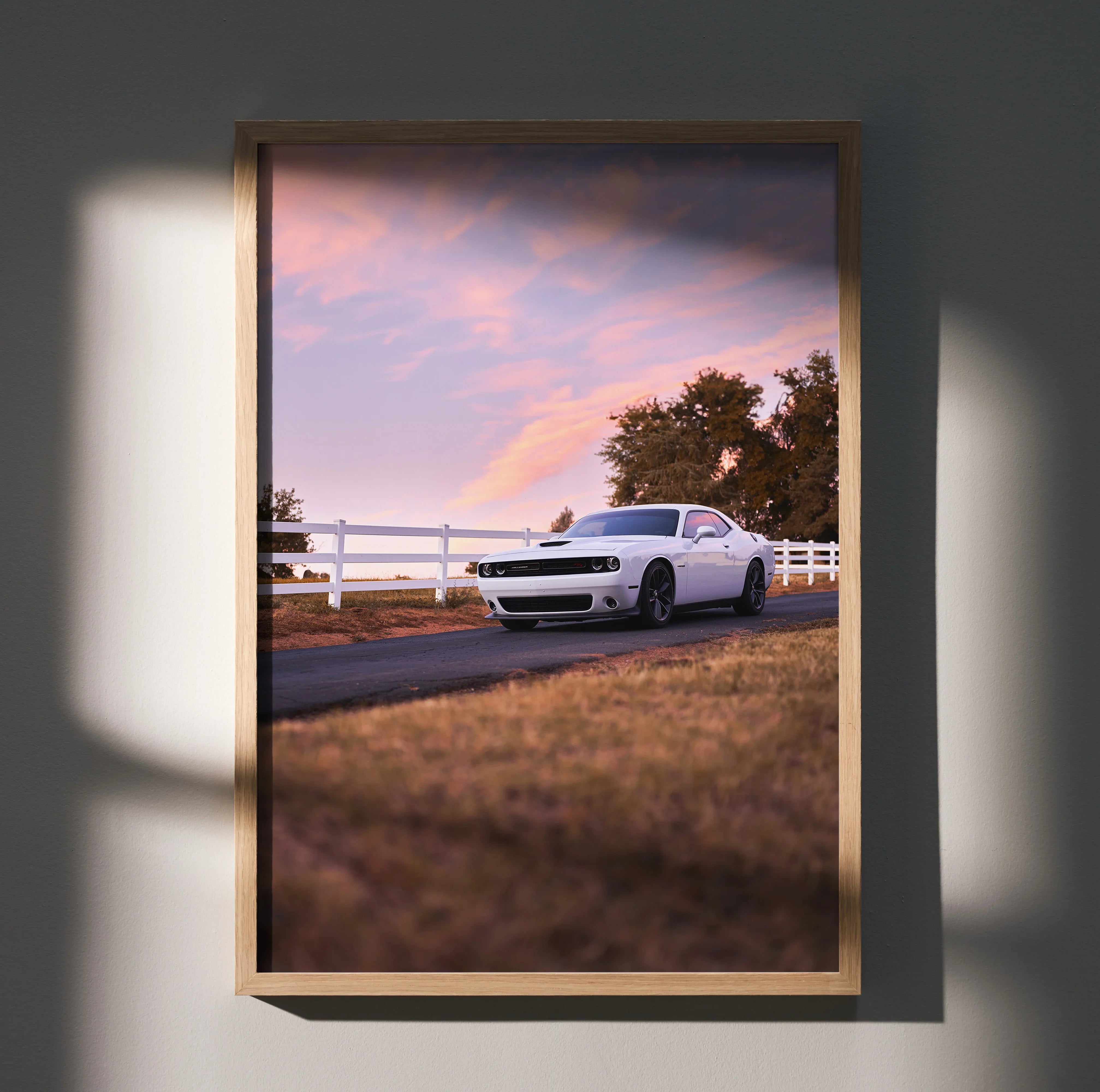 Dodge Challenger parked by white fence at sunset poster wall art in wood frame.