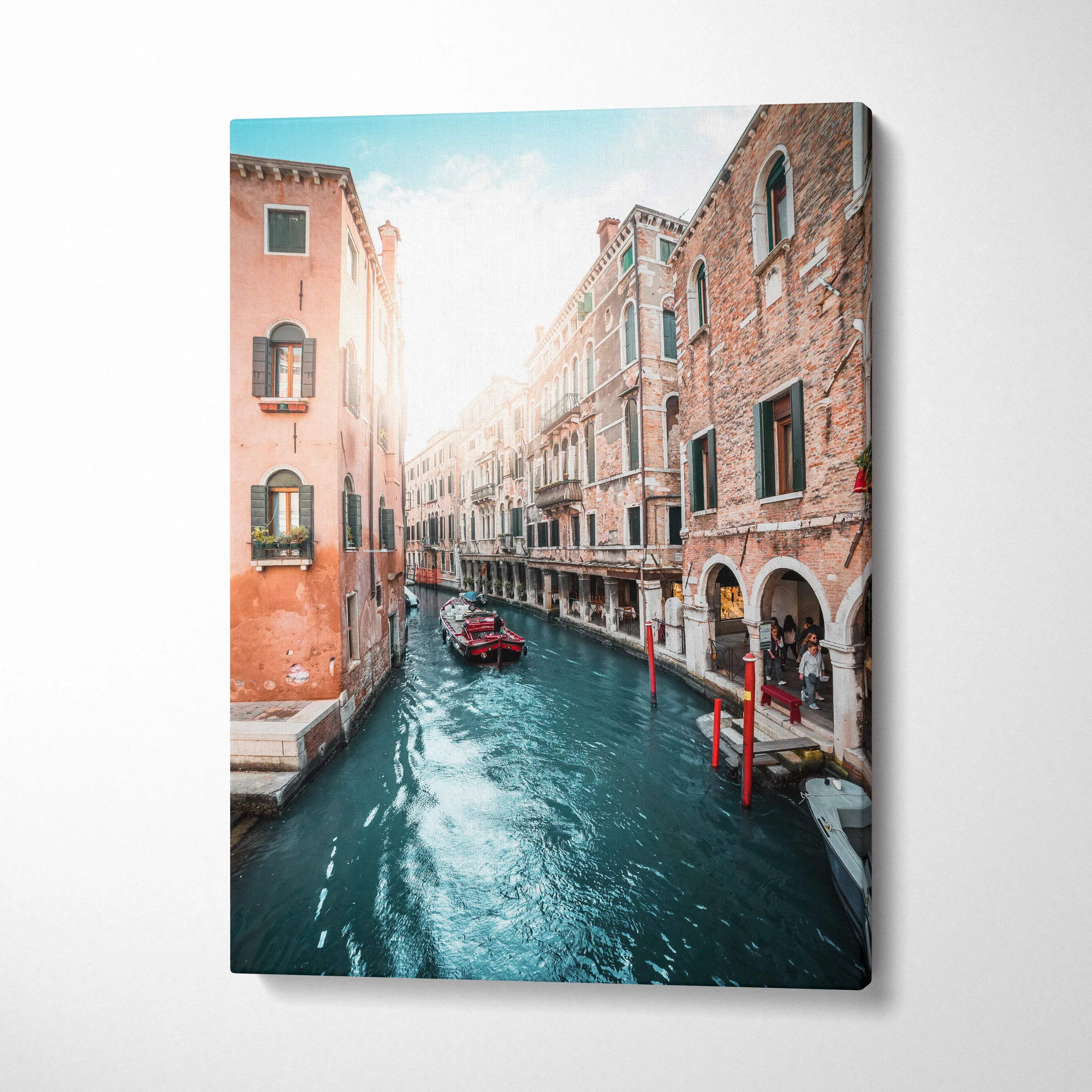 Vertical canvas wall art of a sunlit Venetian canal with historic brick buildings and boats.