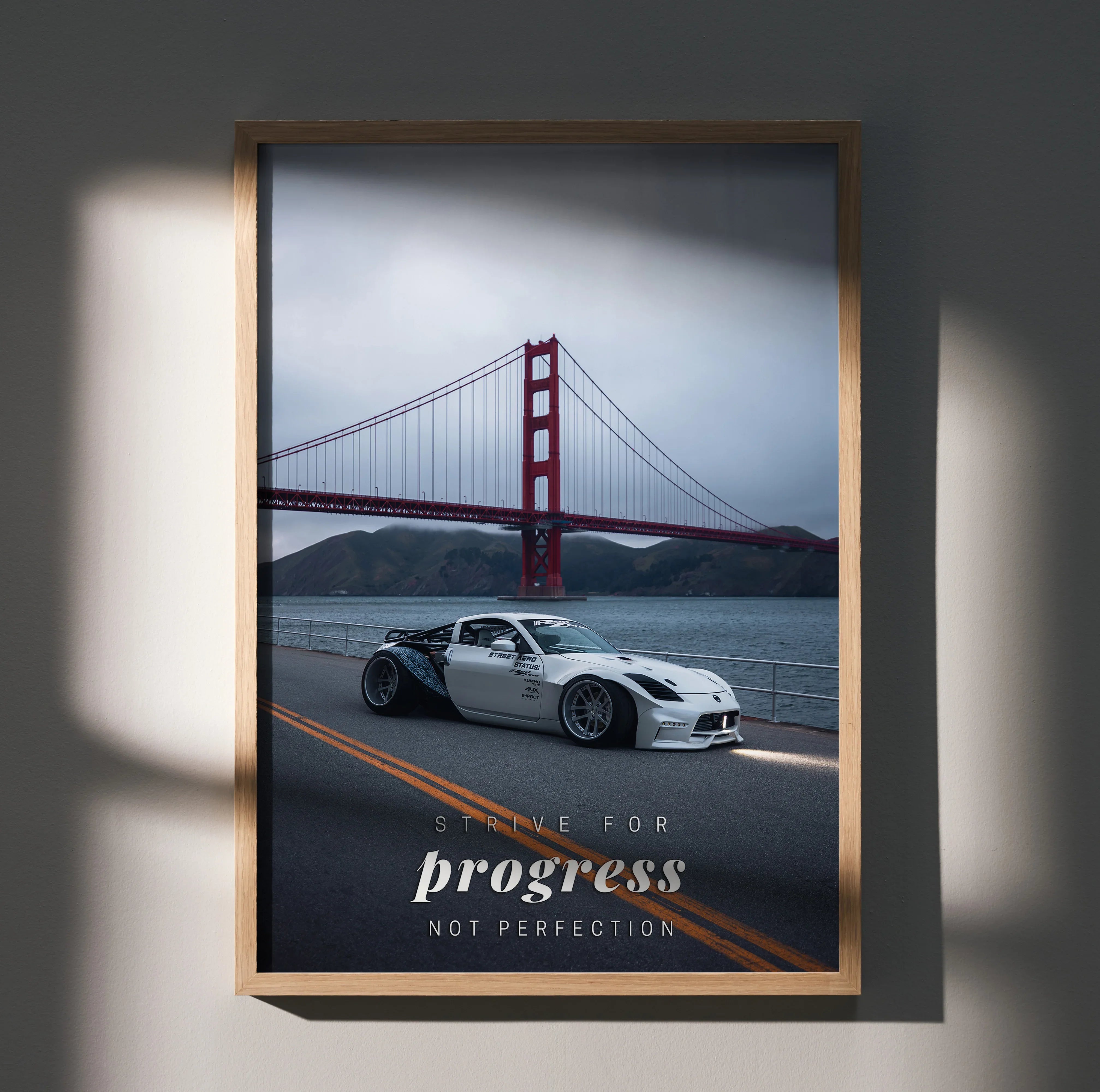 Motivational poster wall art with white Nissan 350Z on road and Golden Gate Bridge in background.