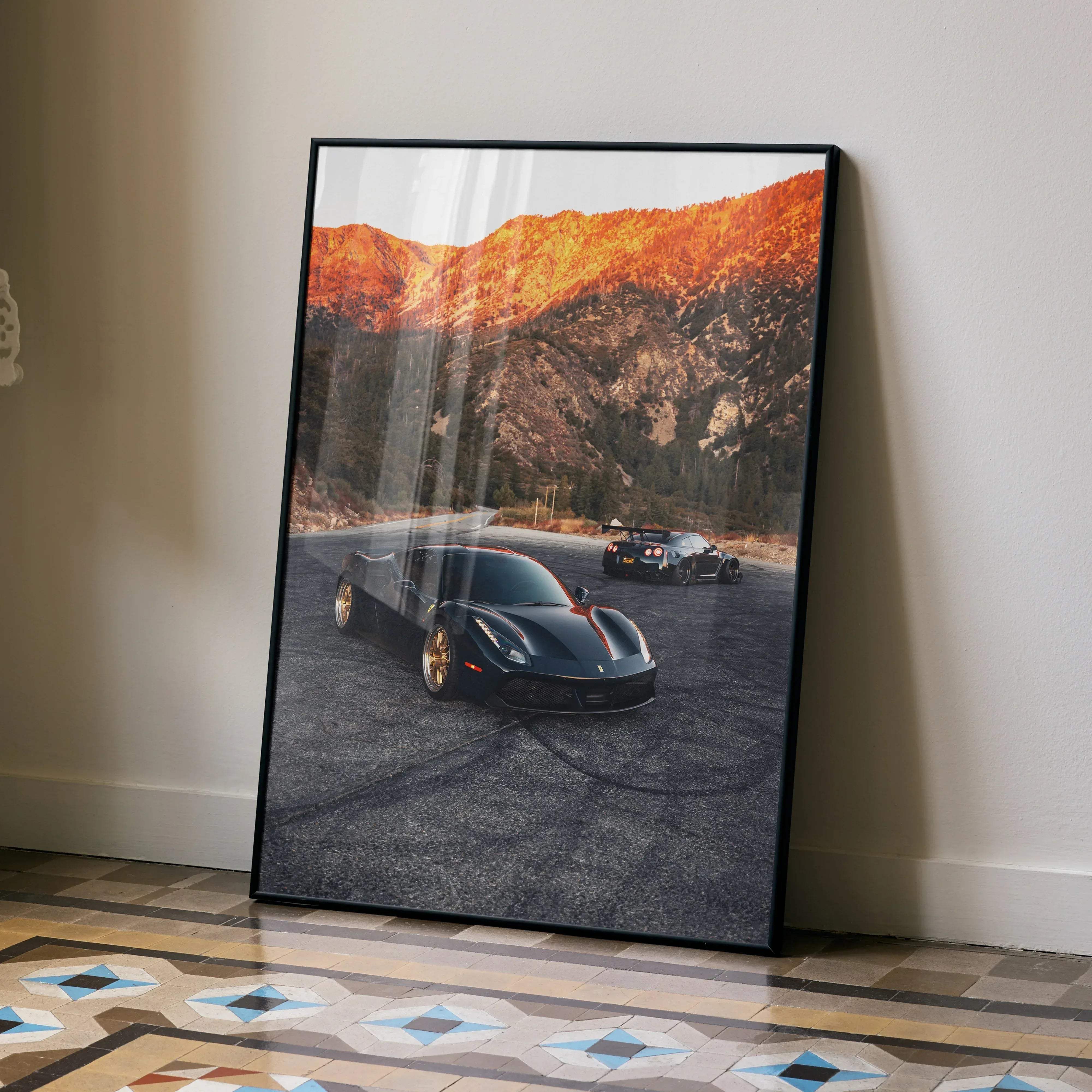Black framed art print of sleek black Ferrari 488 GTB with gold rims and red accents on asphalt road by sunlit mountains