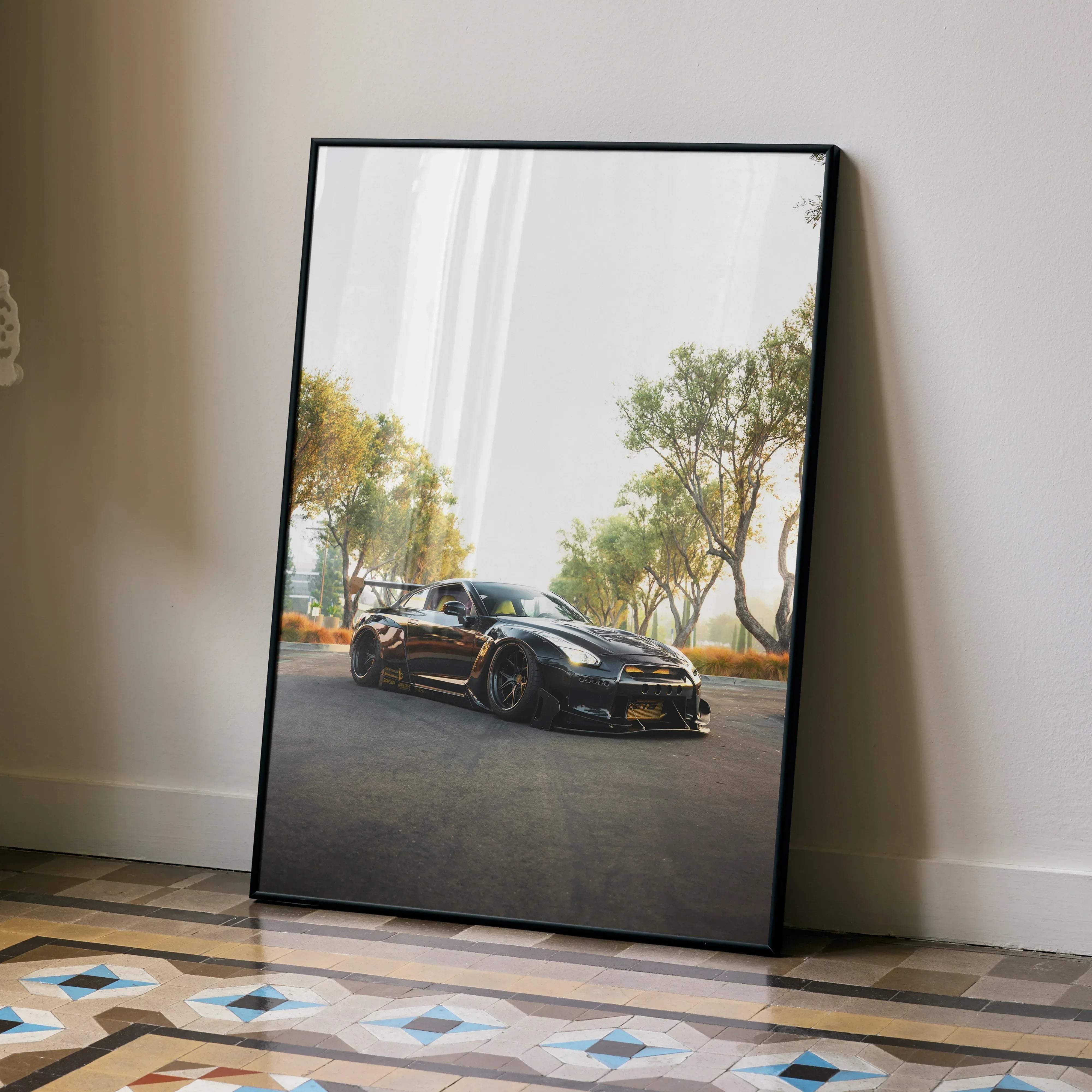 Black framed poster of glossy black nissan gt-r r35 with gold accents and custom wheels leaning against white wall