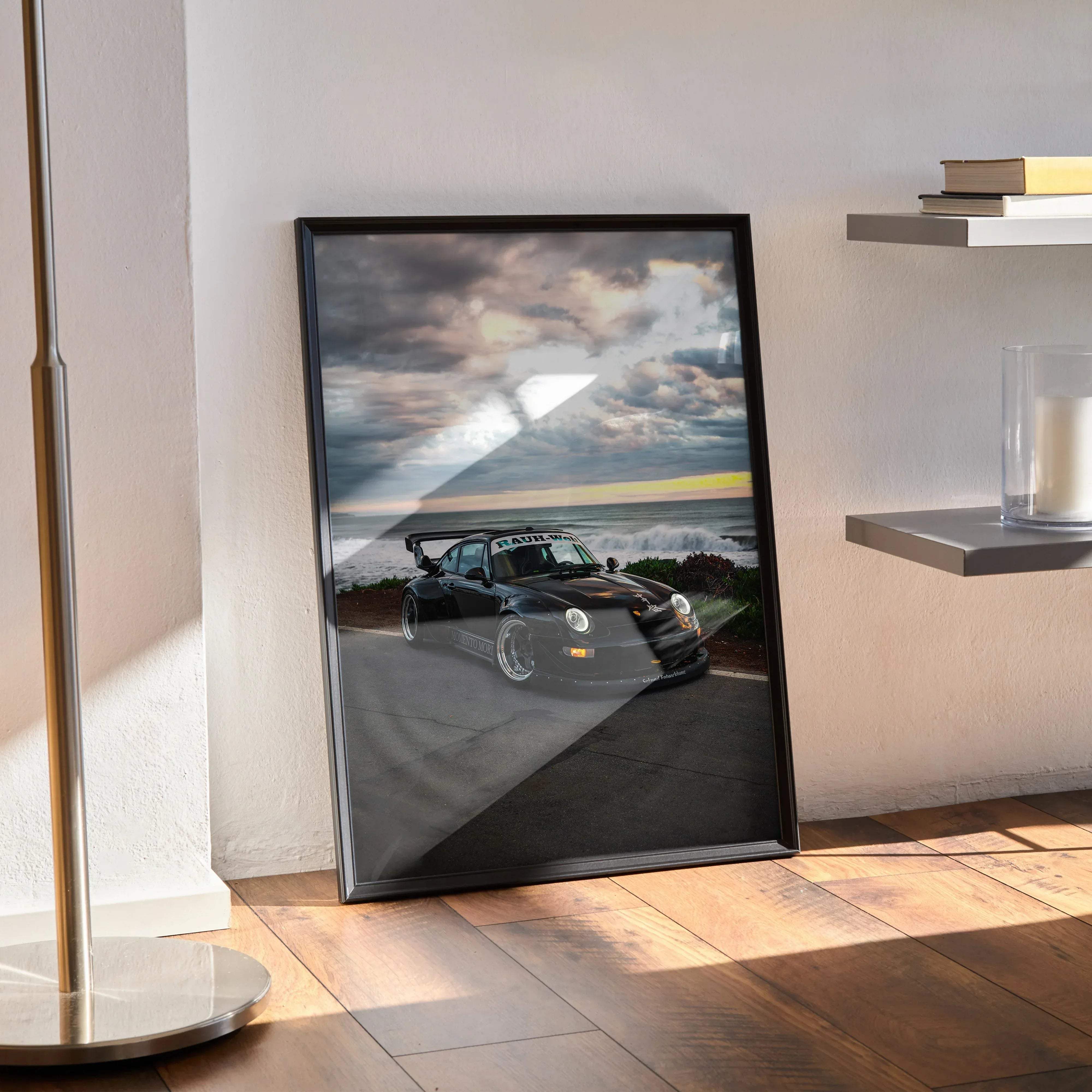 Black framed poster featuring a sleek glossy black porsche 911 with custom wheels speeding on a coastal road